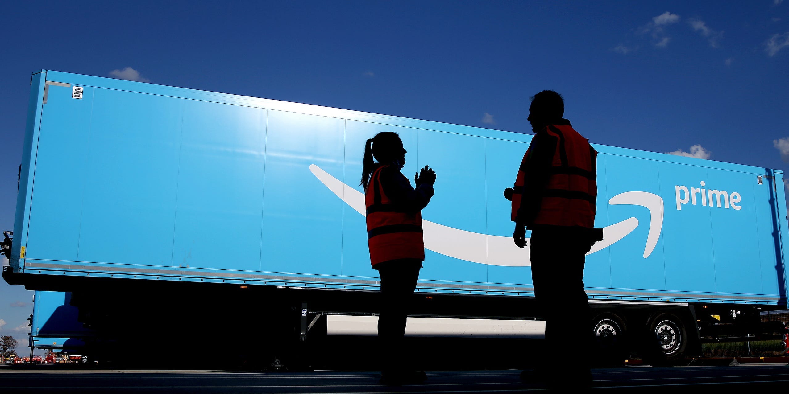 Amazon workers stand in front of a large "Amazon Prime" branded truck trailer.