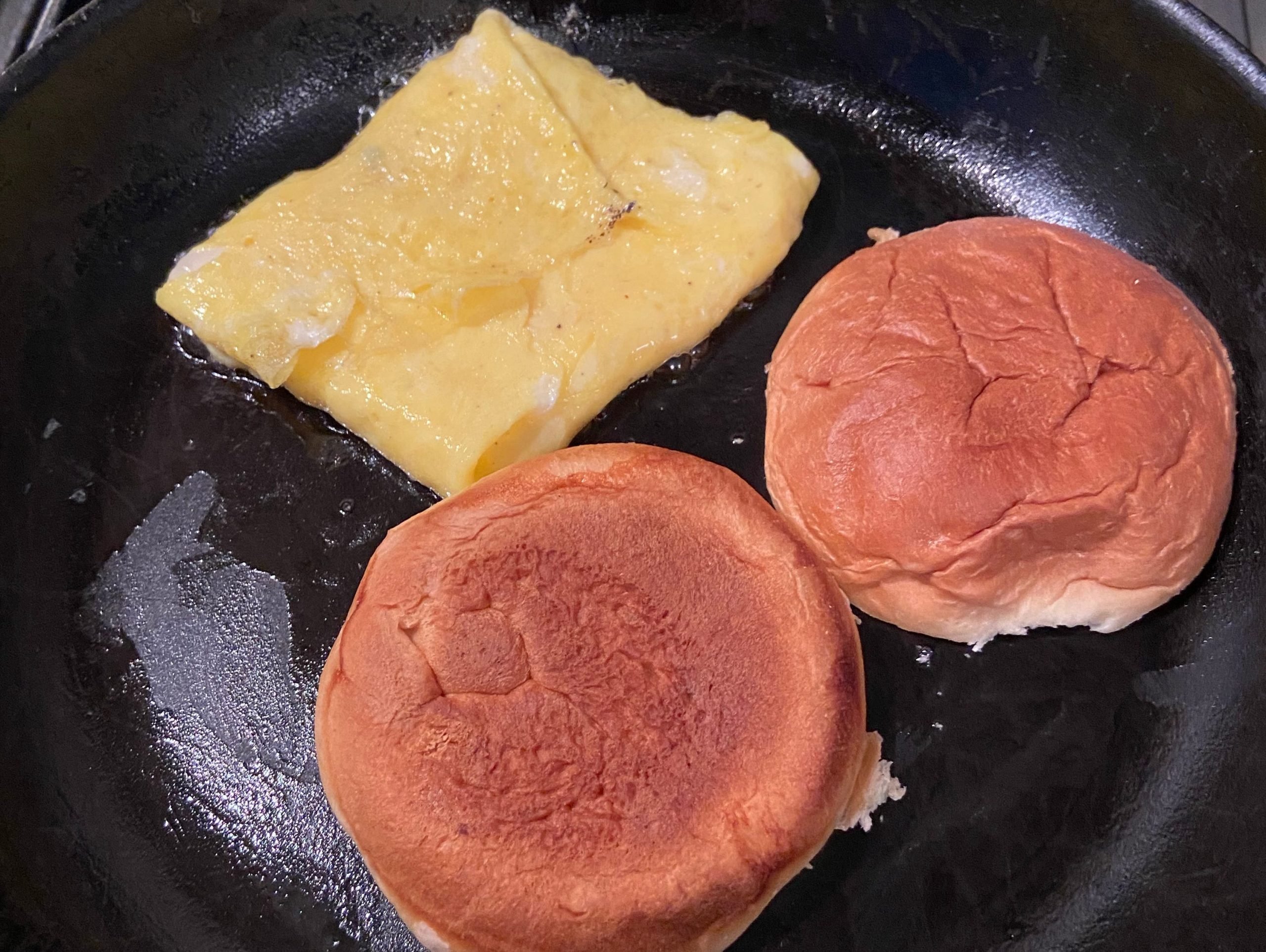 Eggs and hamburger buns on a black pan.