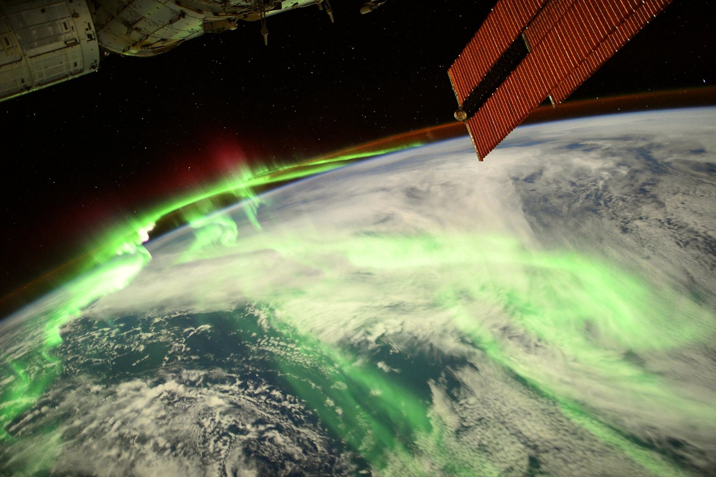 green aurora snaking over earth with space station solar panels in foreground