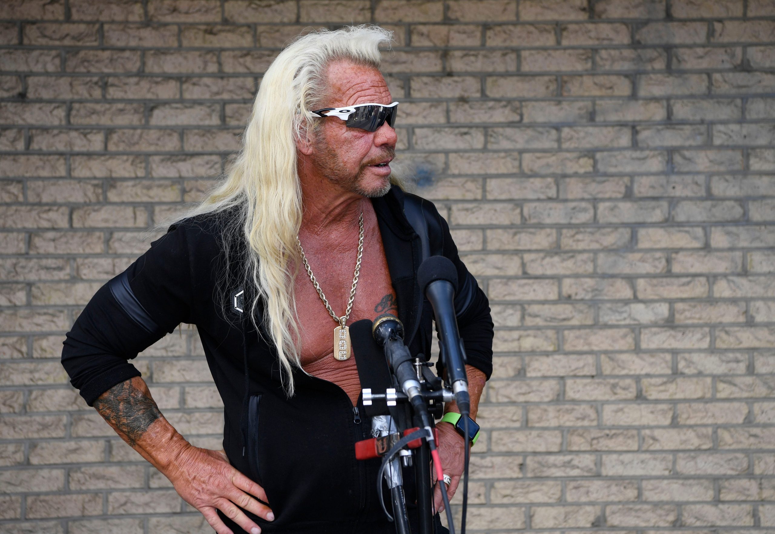 Dog the Bounty Hunter stands in front of a brick wall