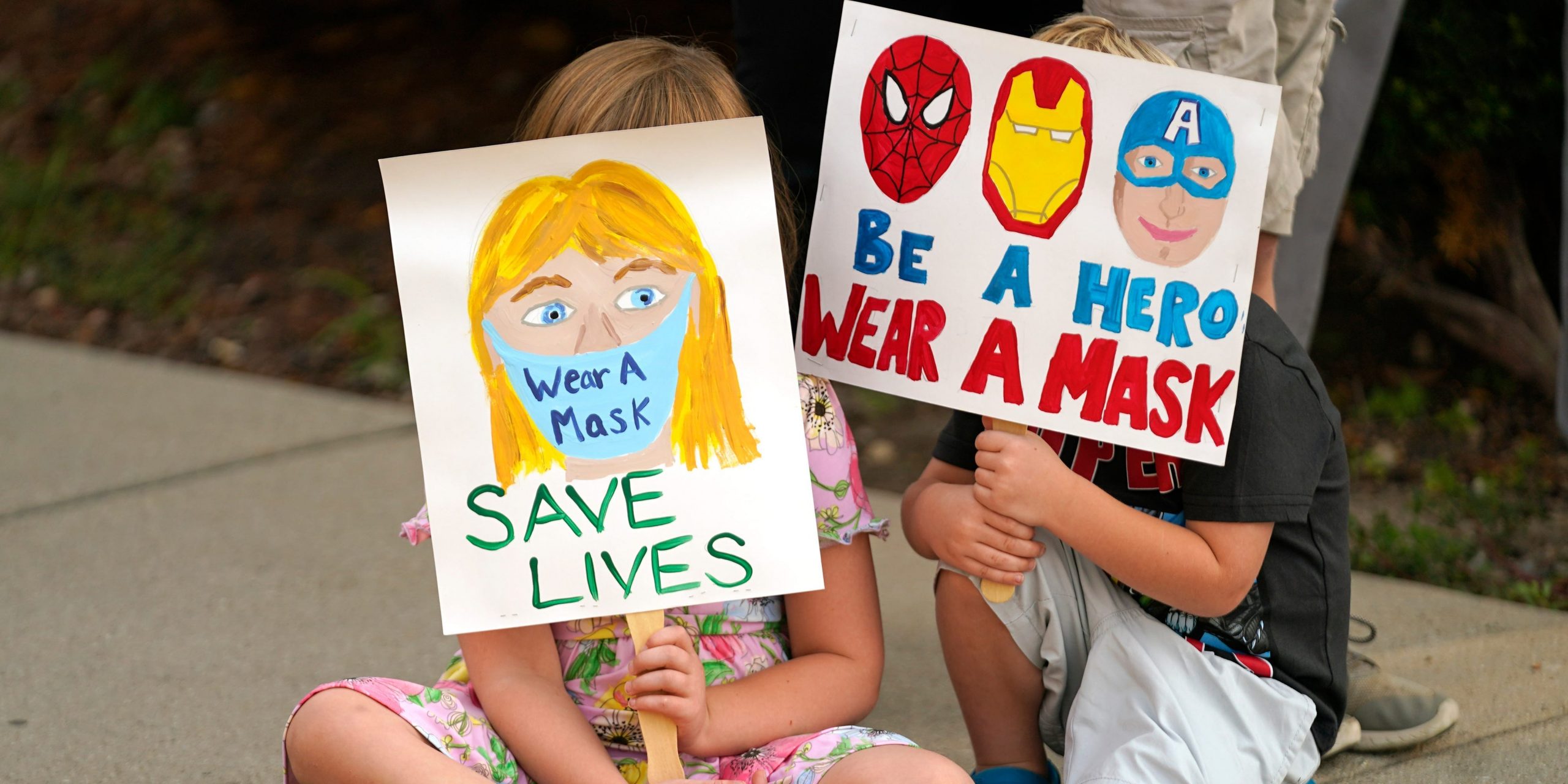 Two kids hold signs encouraging the wearing of masks in the classroom.