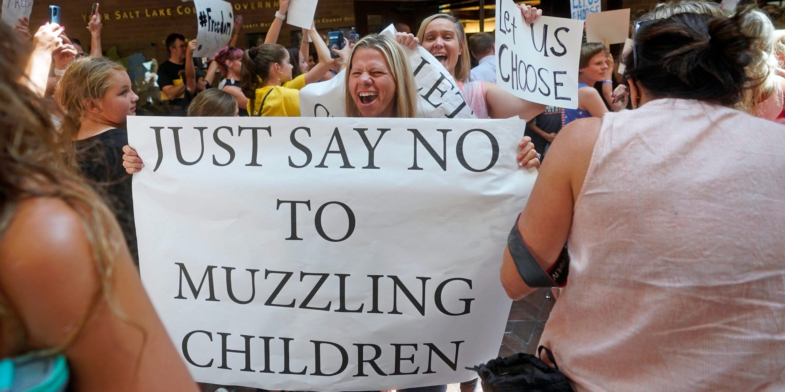 A woman holds a sign that reads: "Just Say No to Muzzling Children."