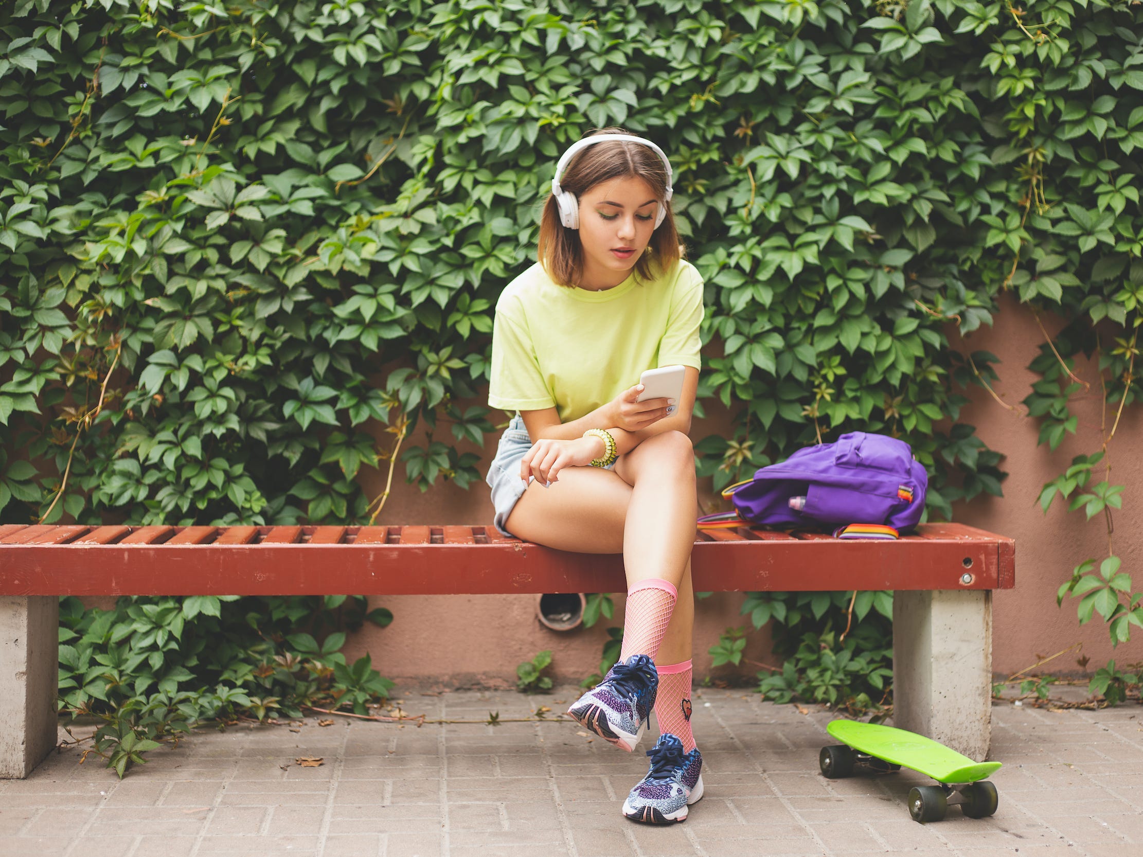 Teen skateboarder using phone with headphones outside