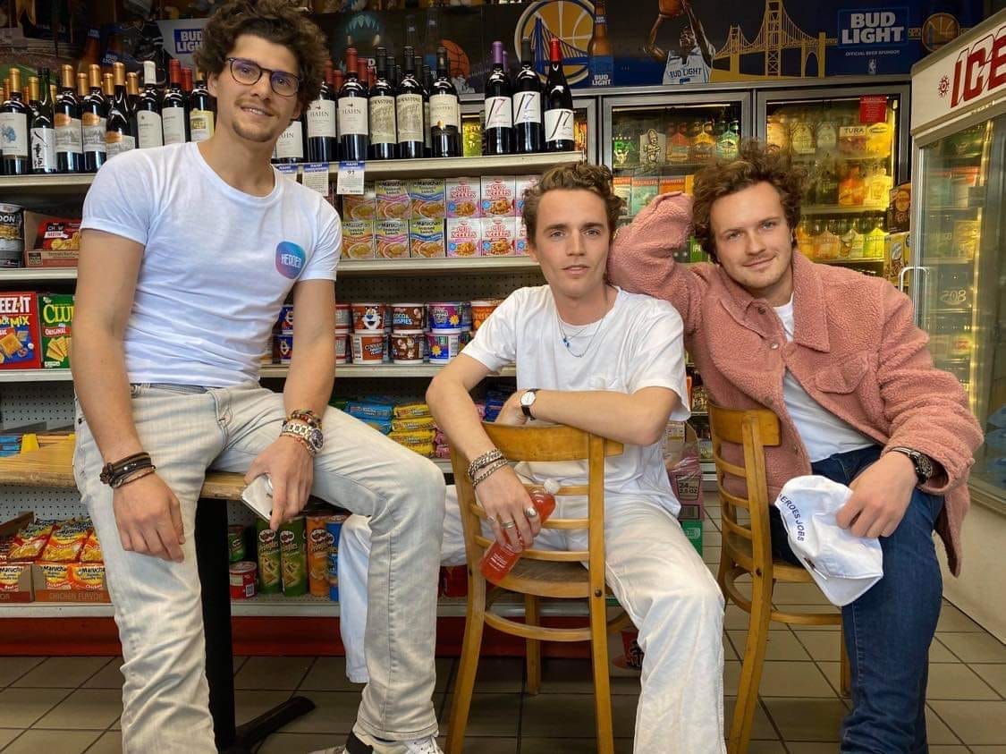 Three men sit in a grocery store looking at the camera smiling