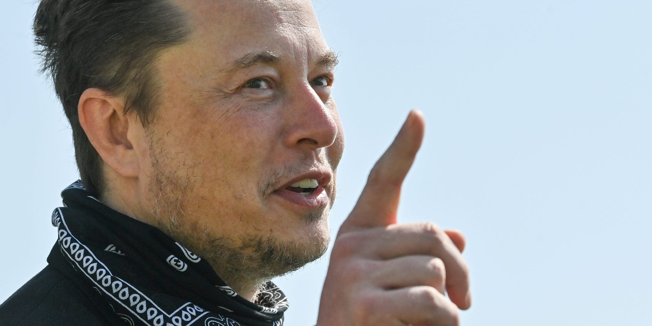 Tesla CEO Elon Musk points a finger upward while wearing a black bandana around his neck