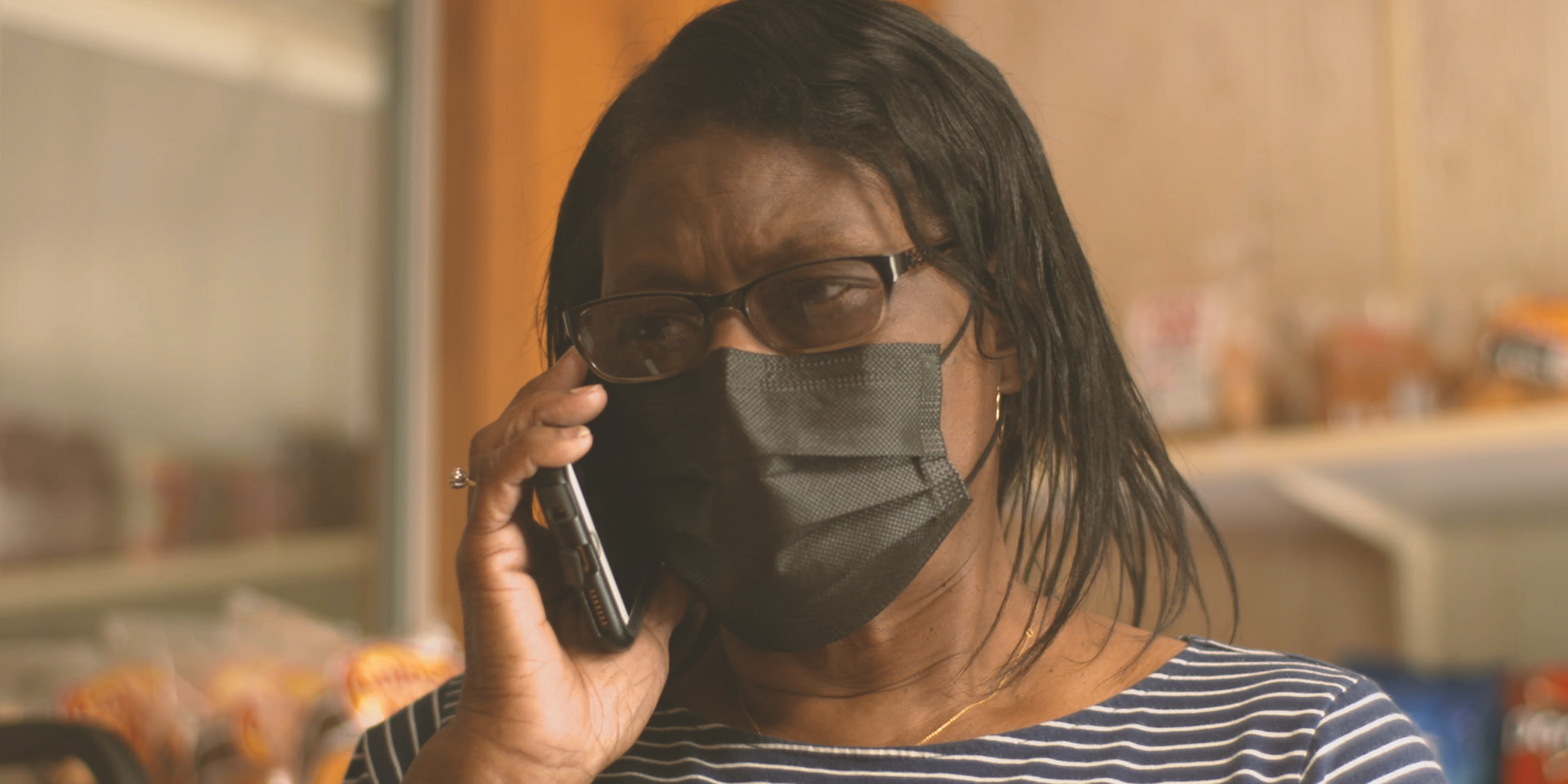 A head-and-shoulders view of a Black woman, Dorothy Oliver, in a mask speaking on the phone.