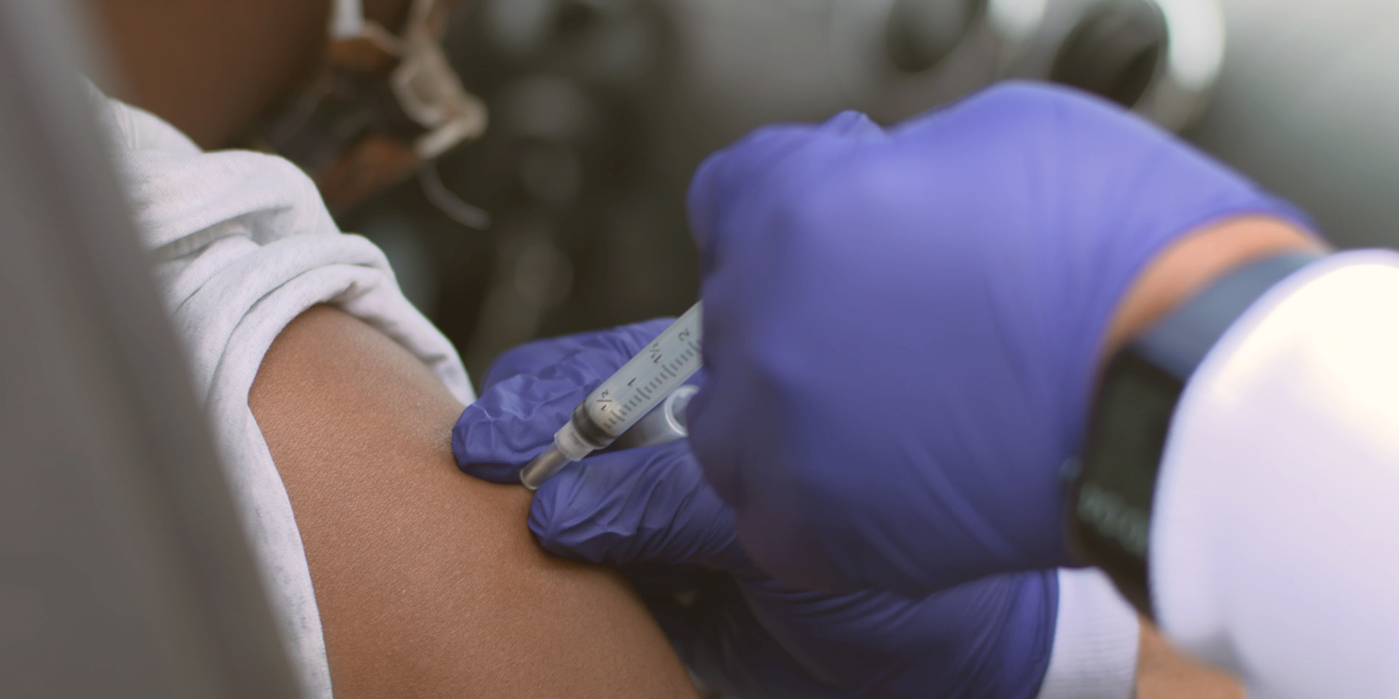 A close-up of a hand in a purple medical glove administering the COVID-19 vaccine