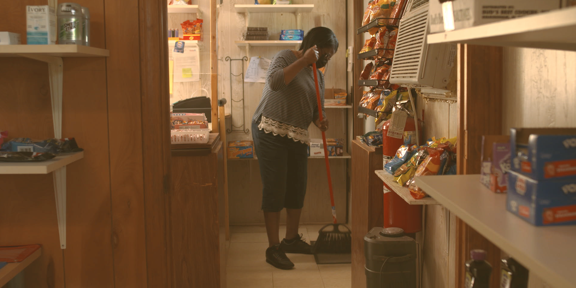 A Black woman, Dorothy Oliver, sweeps the floor in a small grocery store.