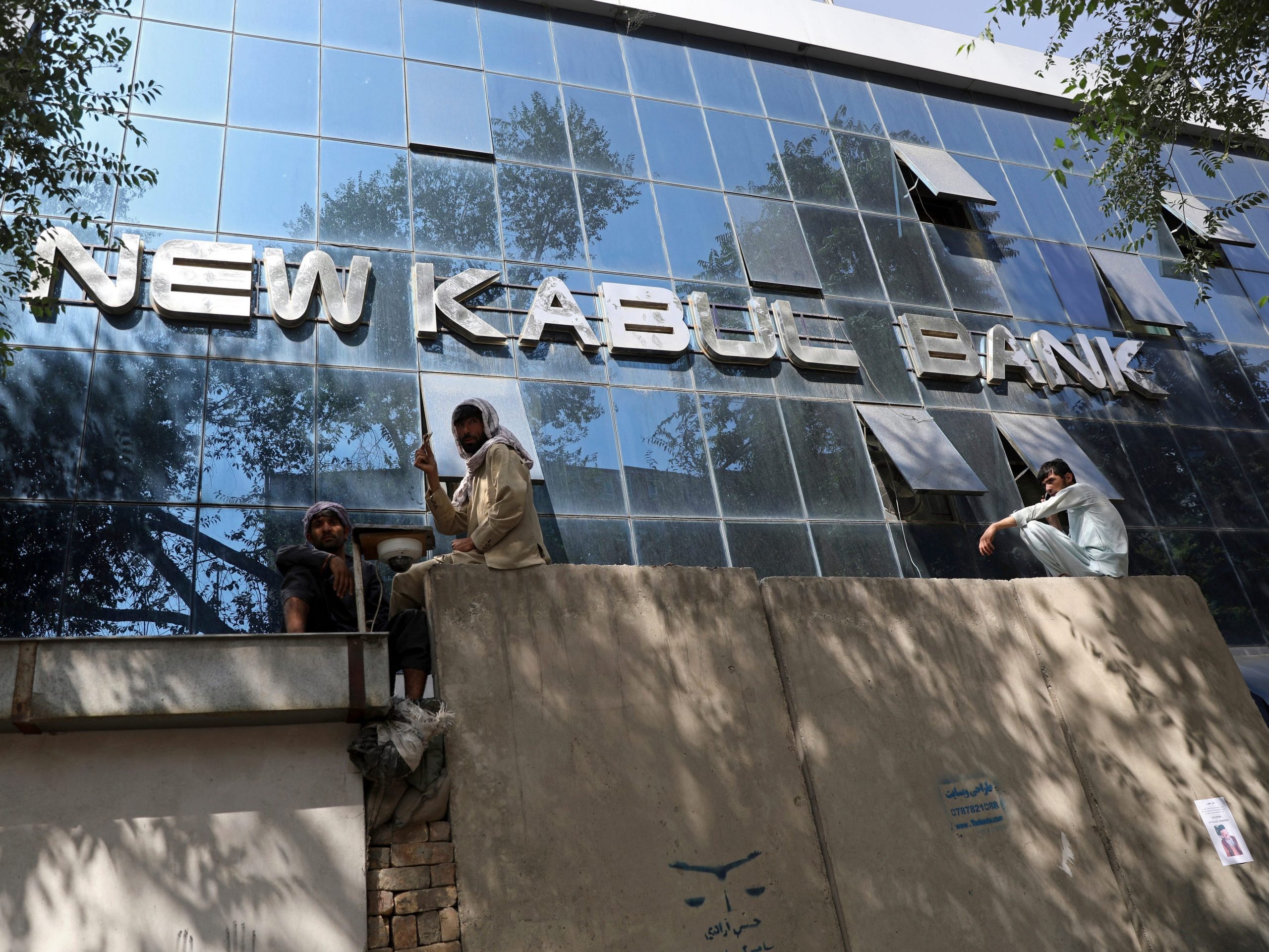 Afghans sit on a wall outside New Kabul Bank waiting to withdraw cash