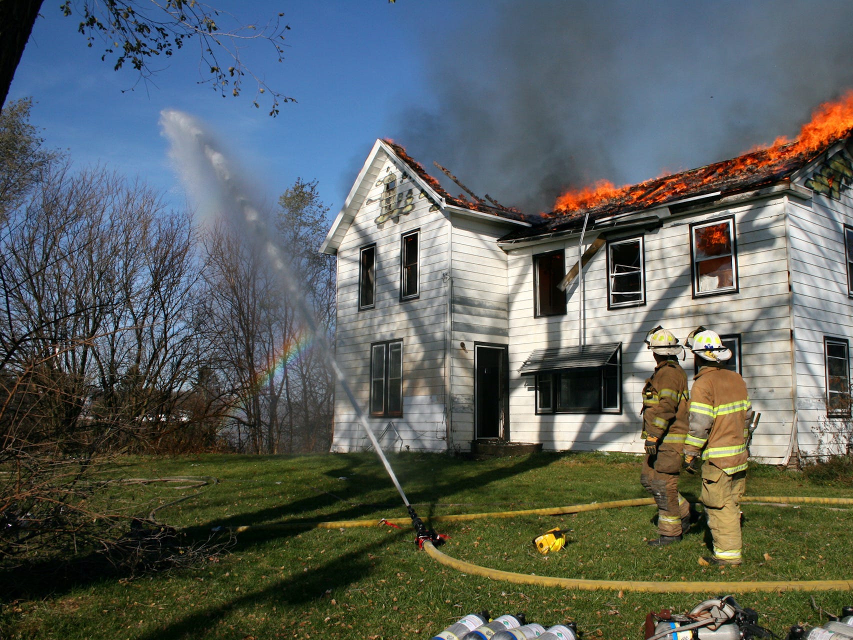 House on fire with firemen and a hose.