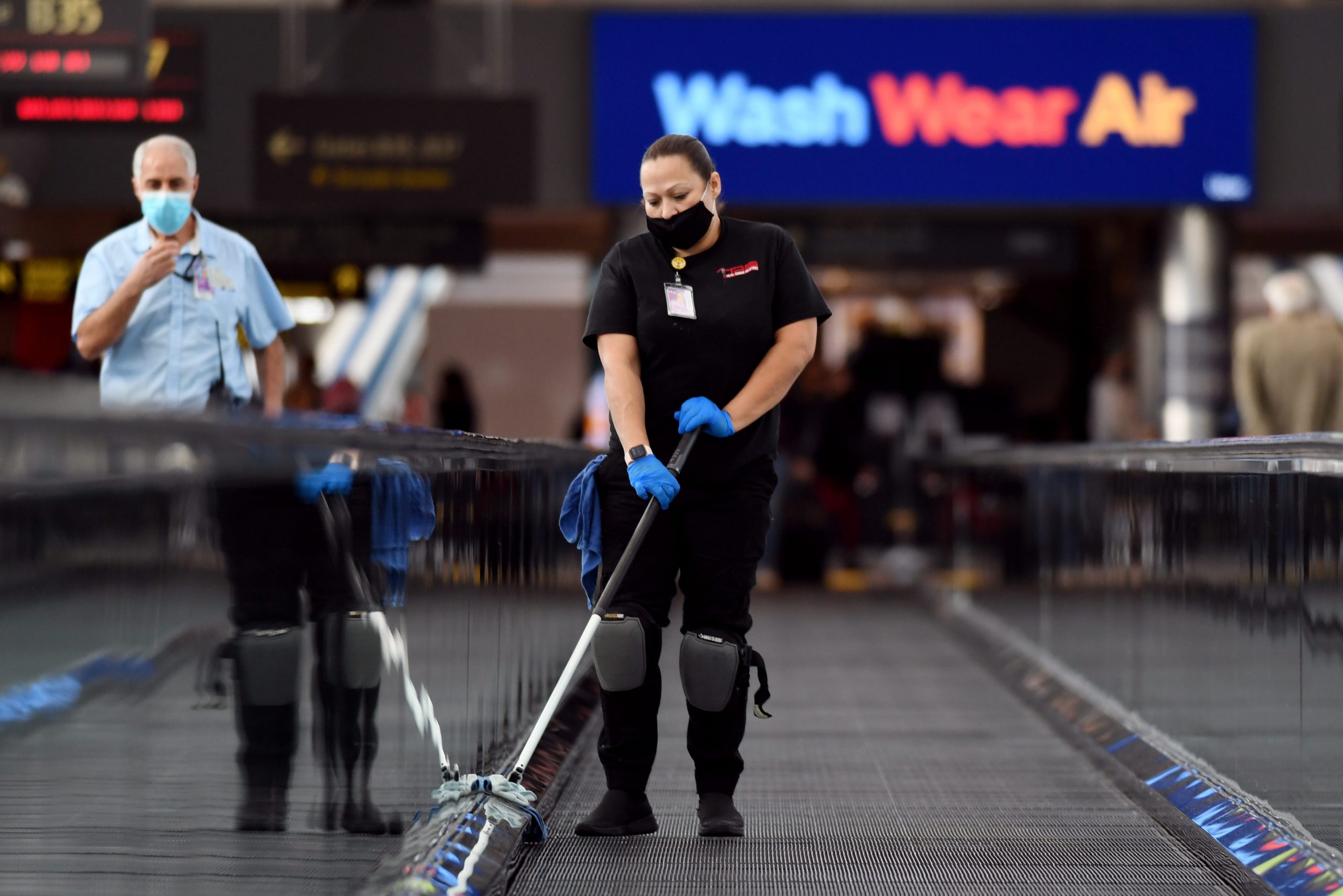 Janitor Mayra Hernandez, right, wiping hand rails at Concourse B of Denver International Airport in Denver, Colorado
