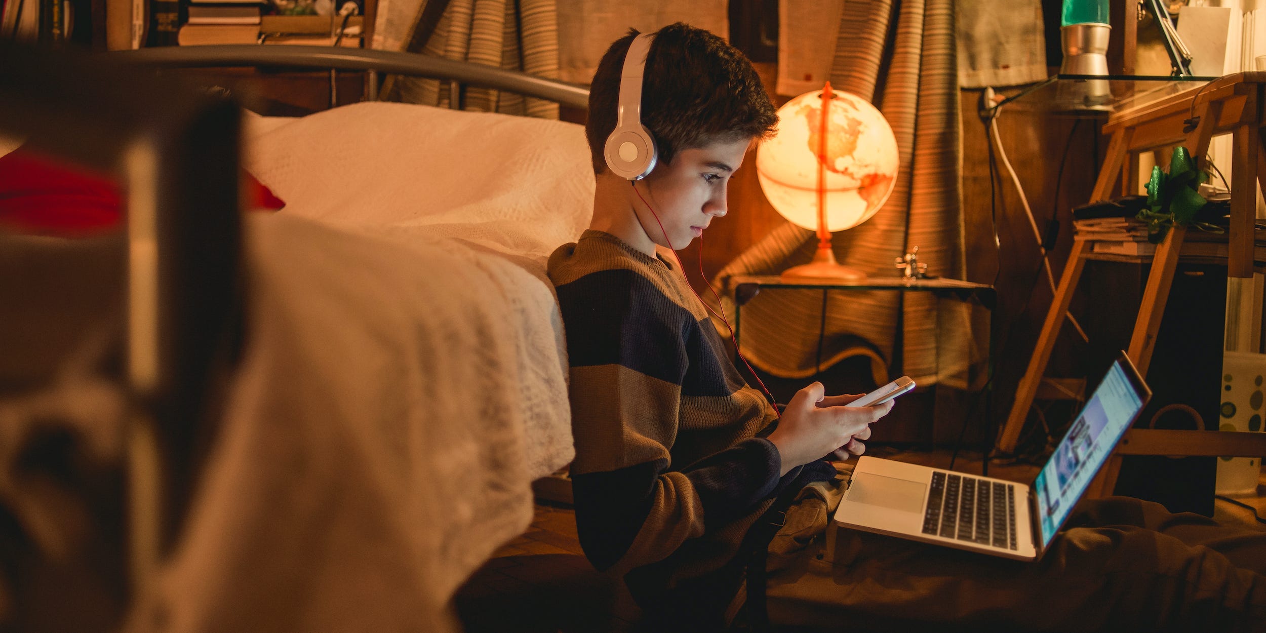 kid using laptop and phone with headphones on at home