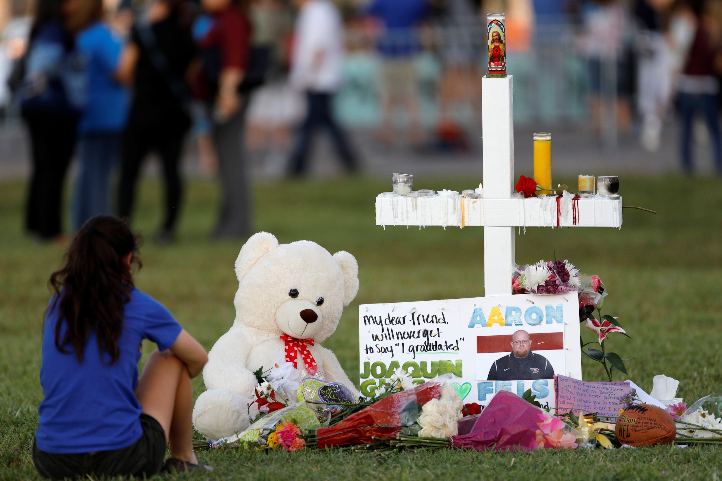 A mourner sits by a cross adorned with pictures of victims, along with flowers and other mementoes, at a memorial two days after the shooting at Marjory Stoneman Douglas High School in Parkland, Florida, U.S. February 16, 2018.