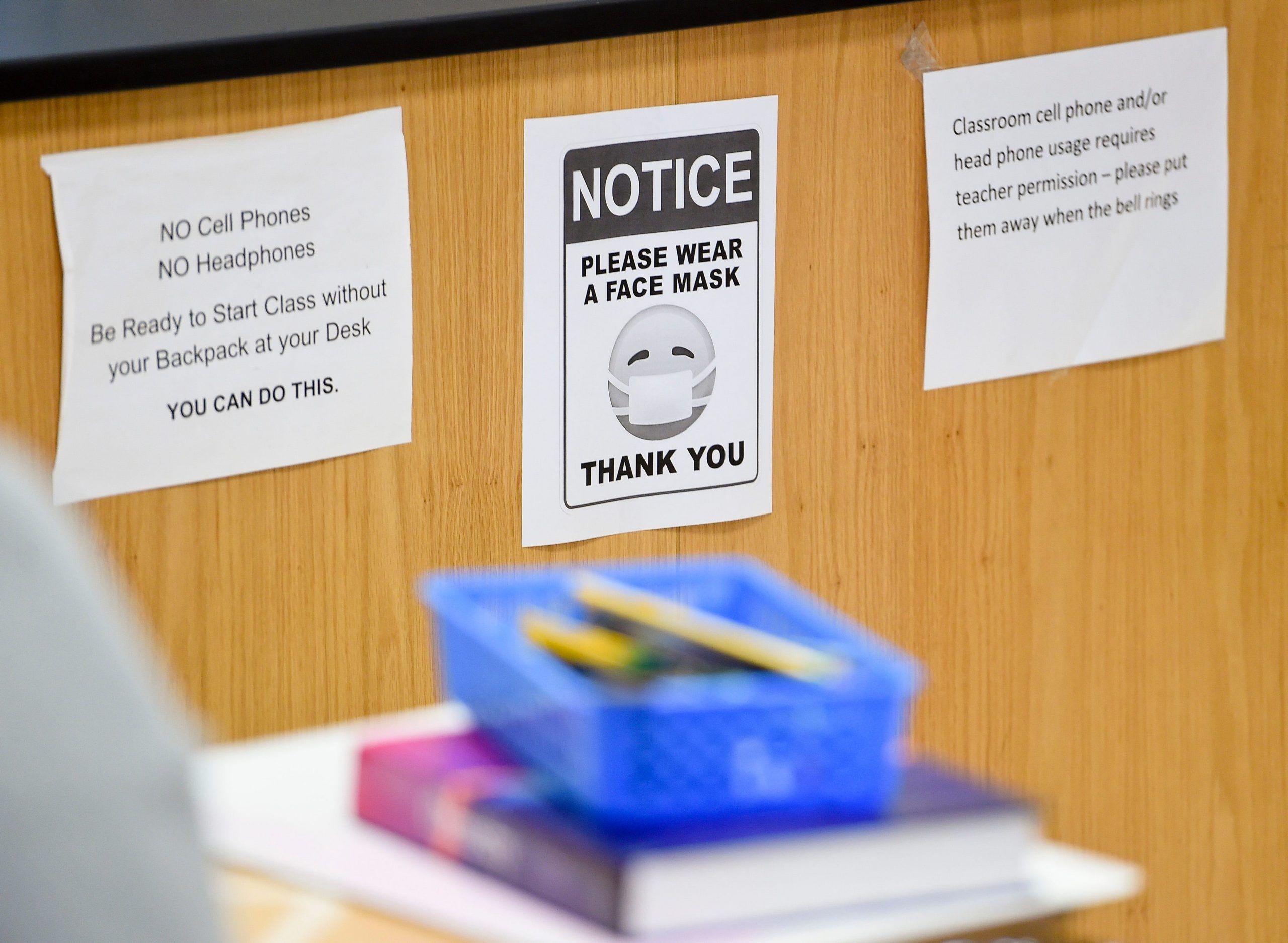 A sign reads 'Please wear a face mask' in a classroom.