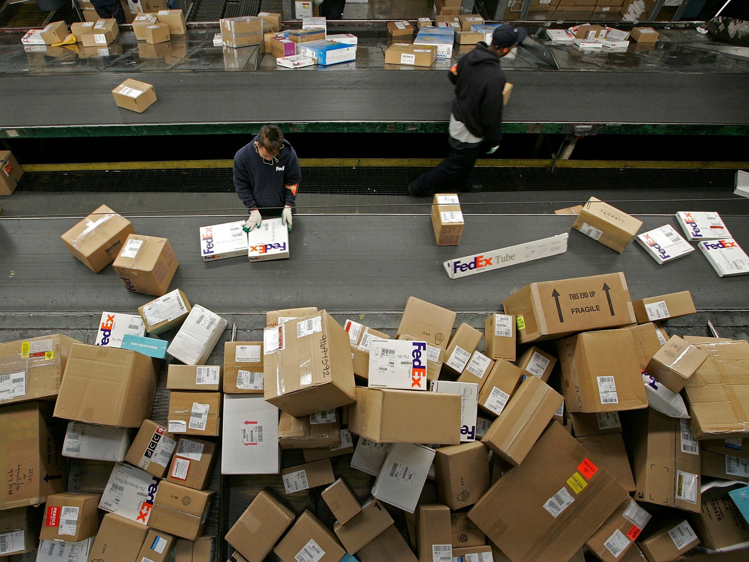 A FedEx worker sorts packages being unloaded from a truck on a conveyor belt at the FedEx Oakland Airport sort facility