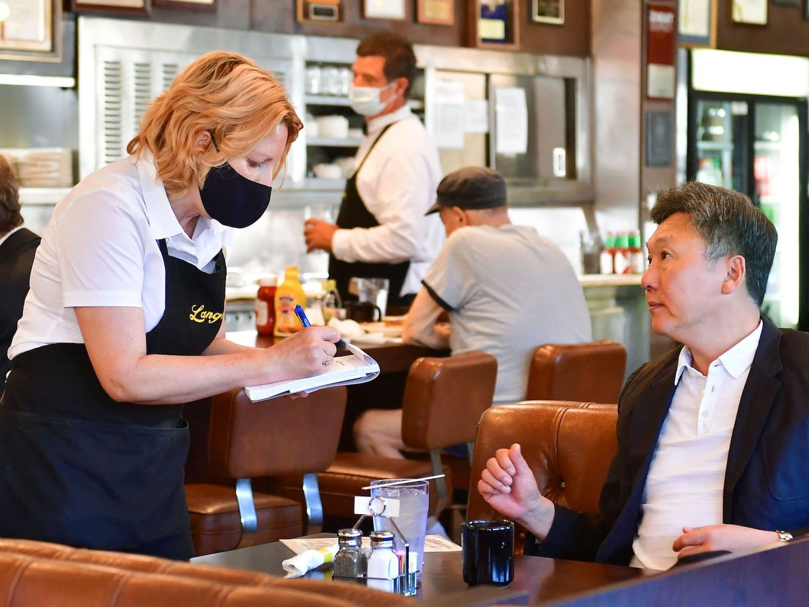 A waitress is taking a customer’s order at a table. There are other customers and another server in the background.