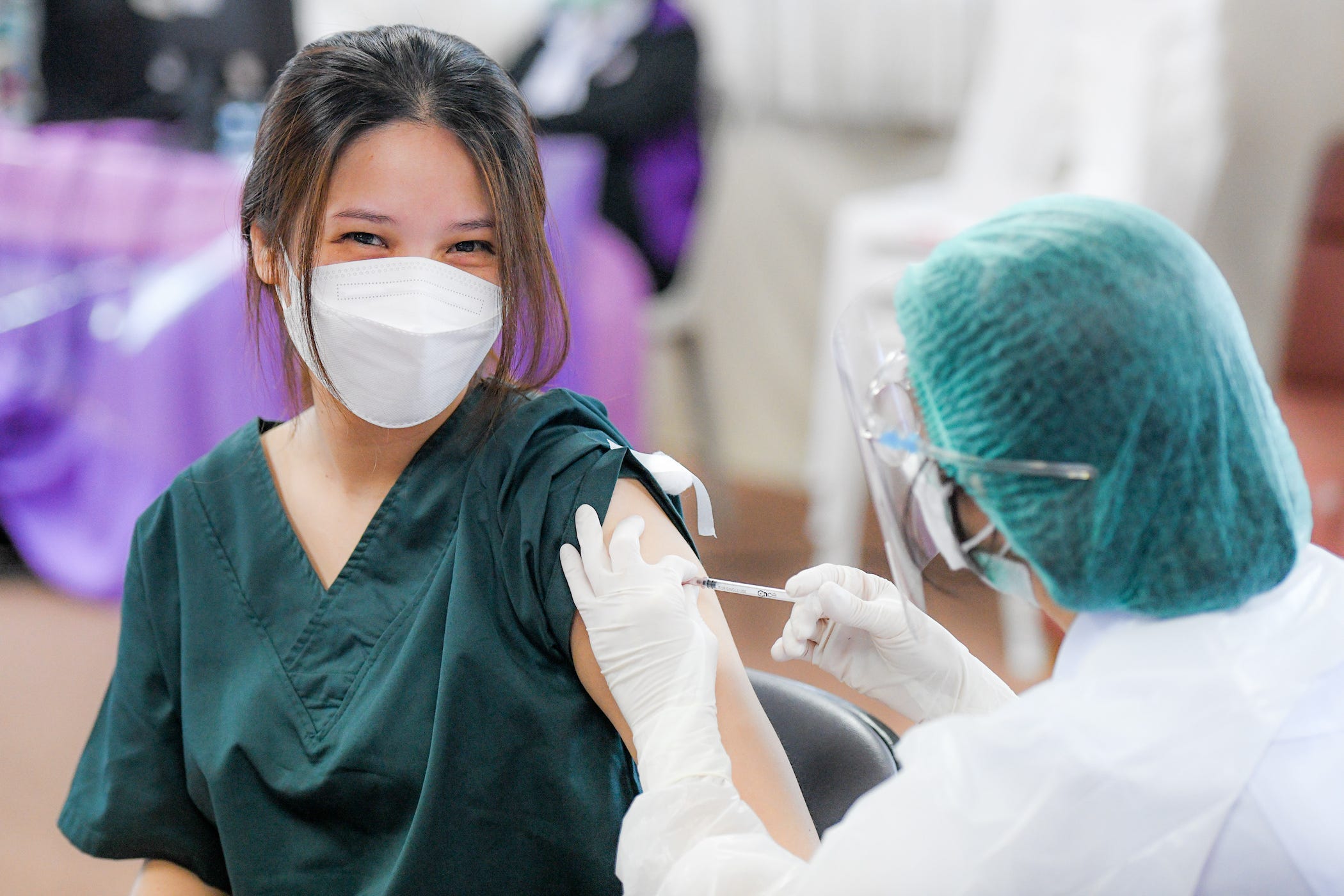 healthcare worker in mask, smiling, getting booster shot.