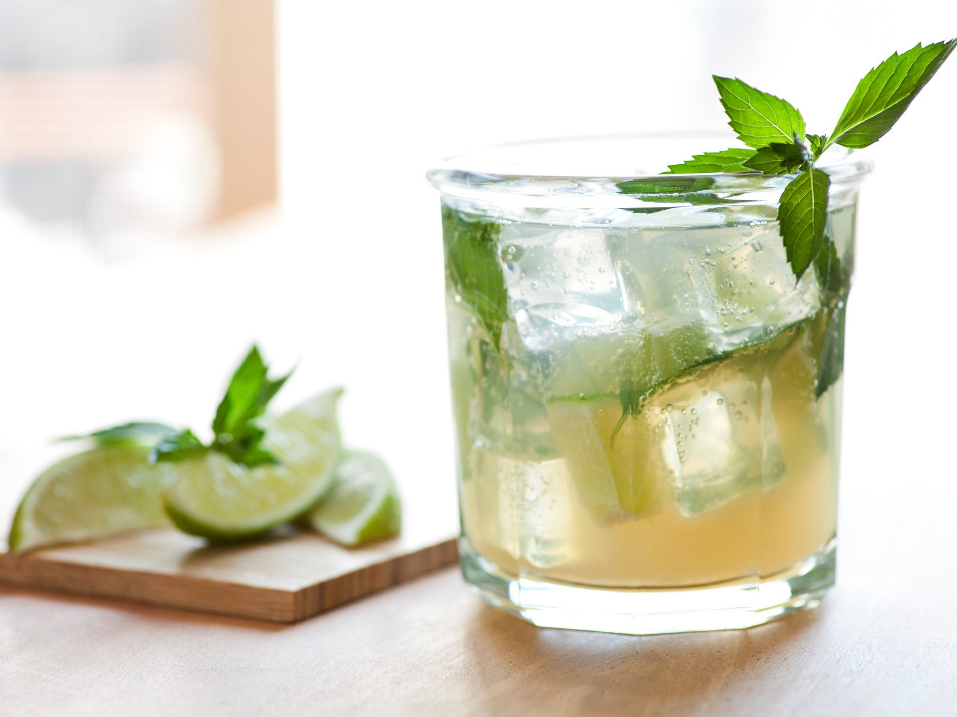 A mojito with some limes next to it.