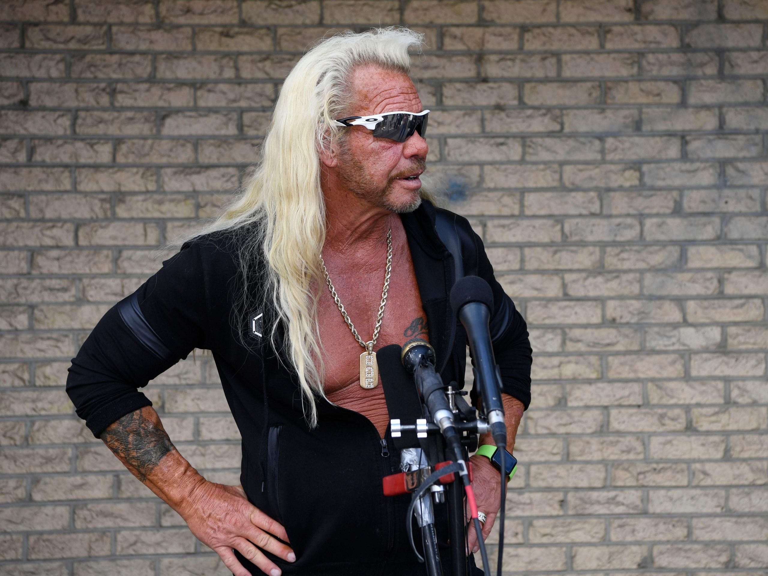 Dog the Bounty Hunter stands in front of a brick wall