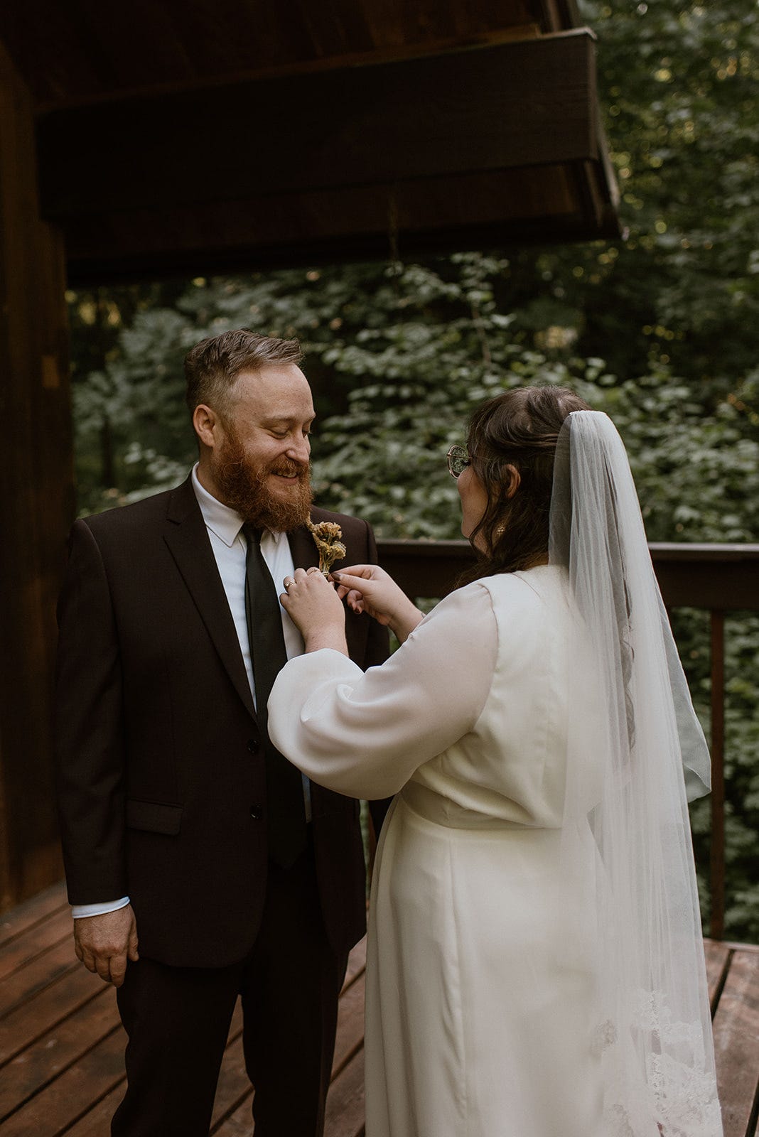 A person in a wedding dressing pinning something onto a person in a black suit