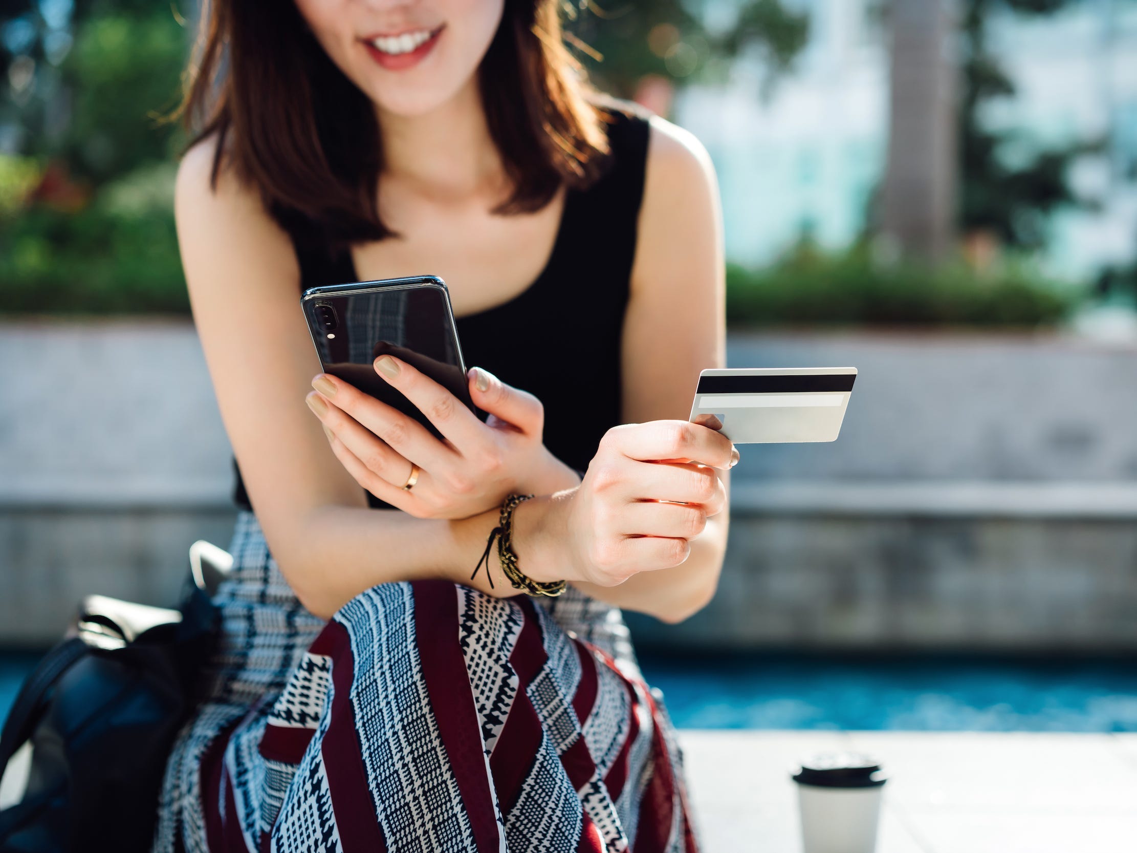 Woman holding credit card and smiling as she shops on her phone