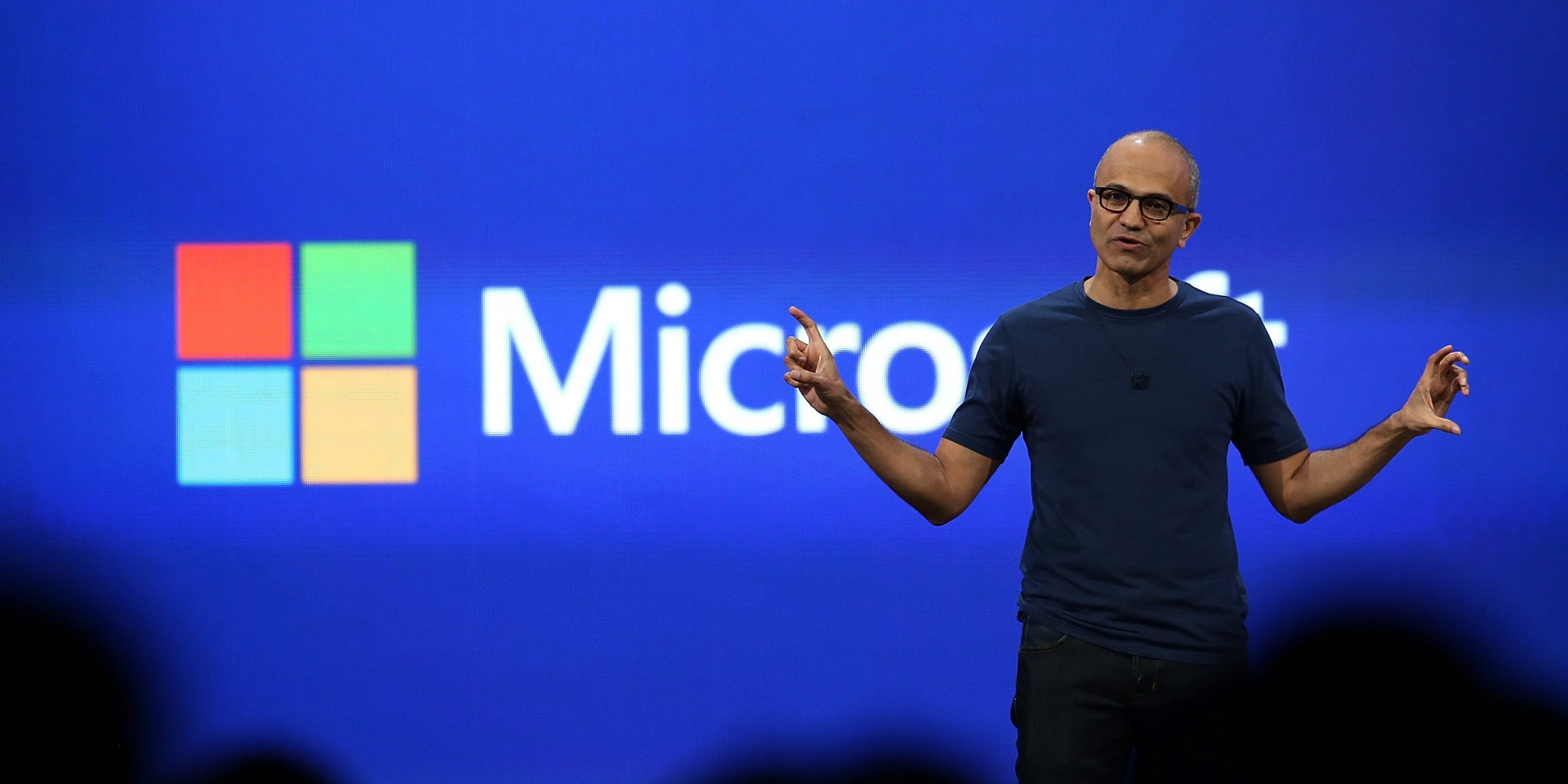 Microsoft CEO Satya Nadella stands on stage and gestures widely with both hands