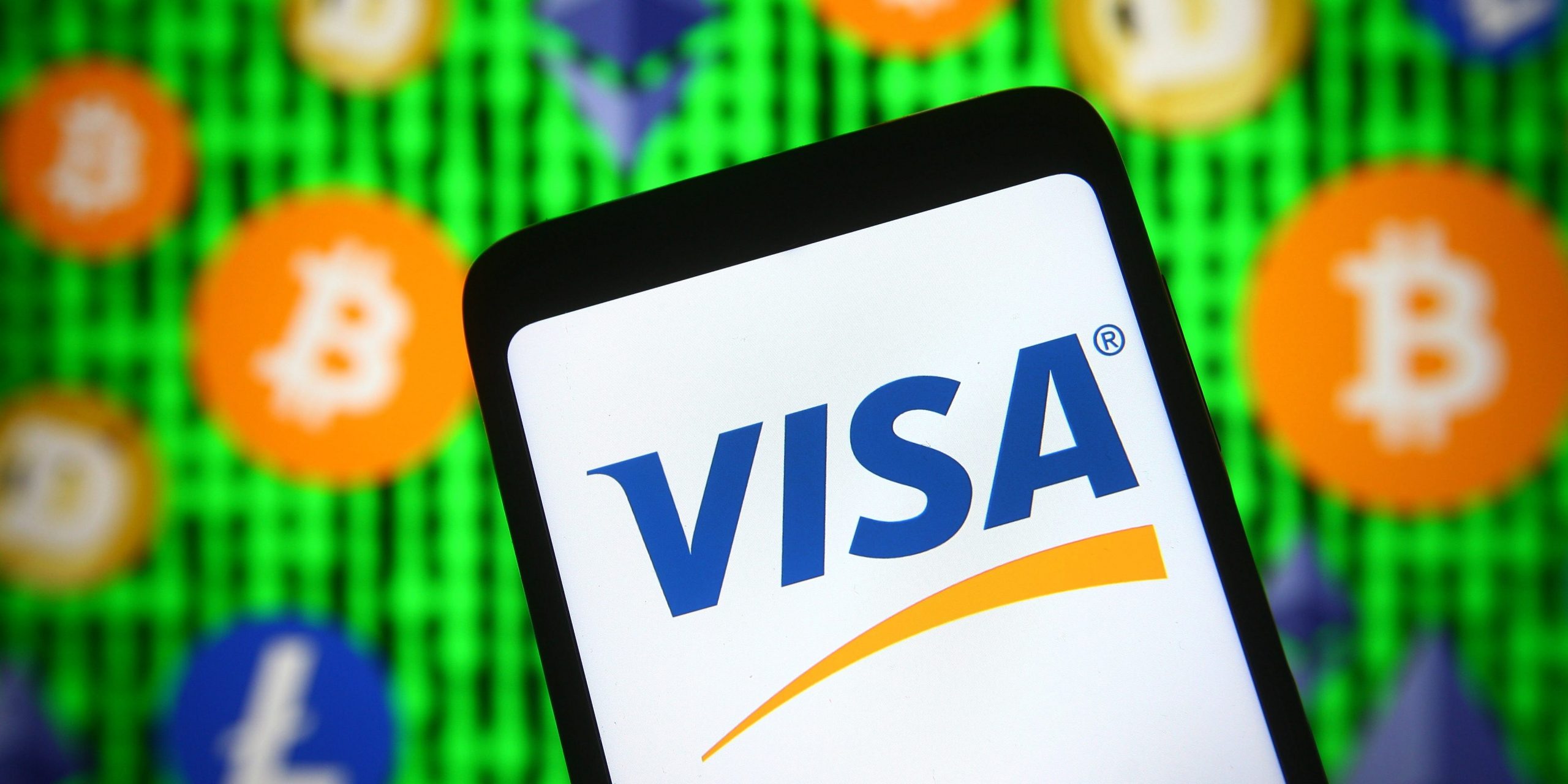 In this photo illustration, Visa logo is seen displayed on a smartphone screen in front of cryptocurrency signs.