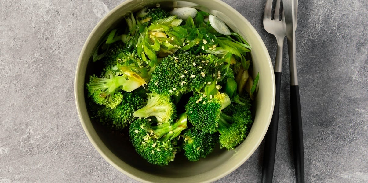 A bowl of steamed broccoli against a gray background.