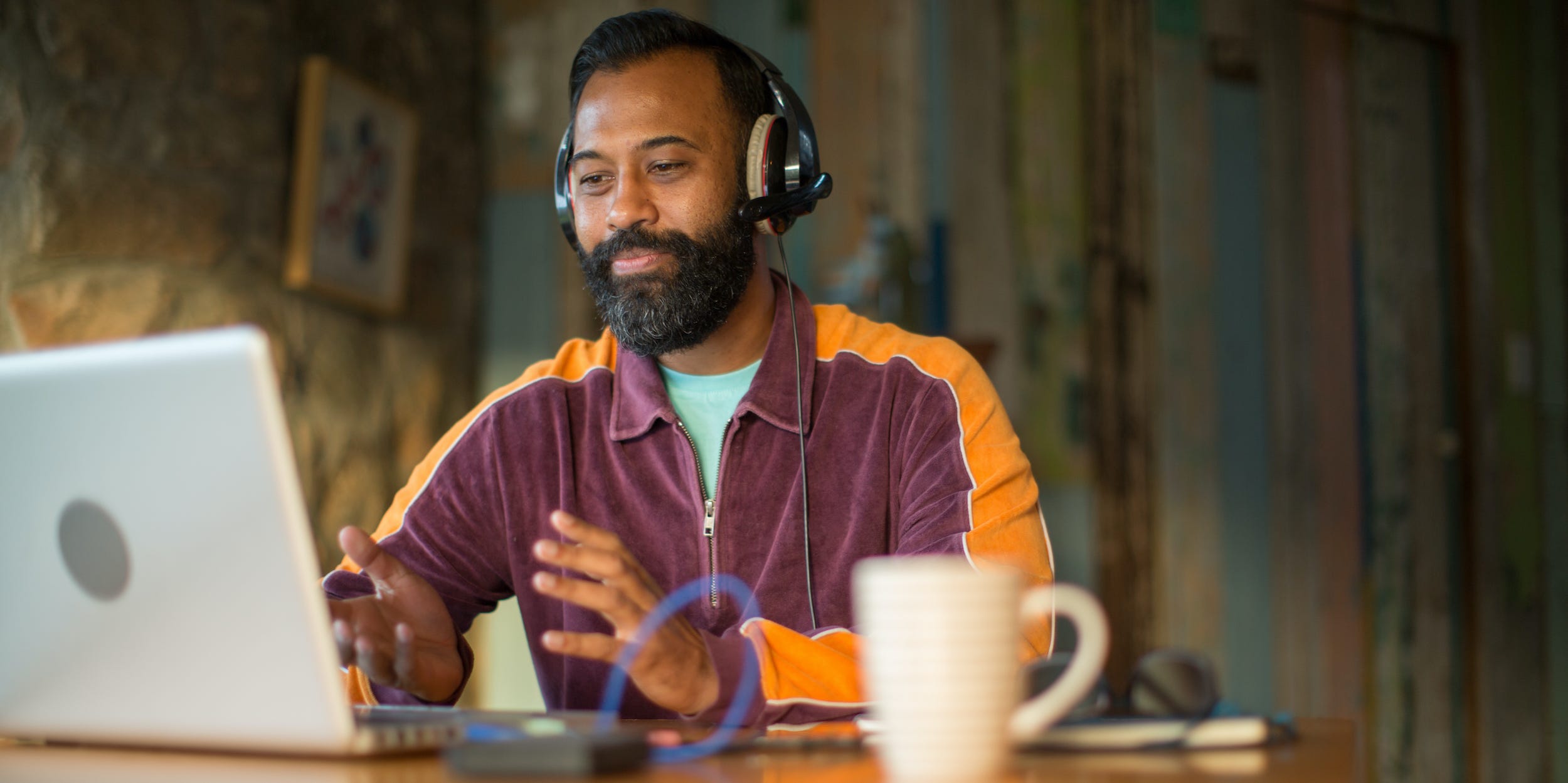 man speaking into laptop computer with headphones on at desk