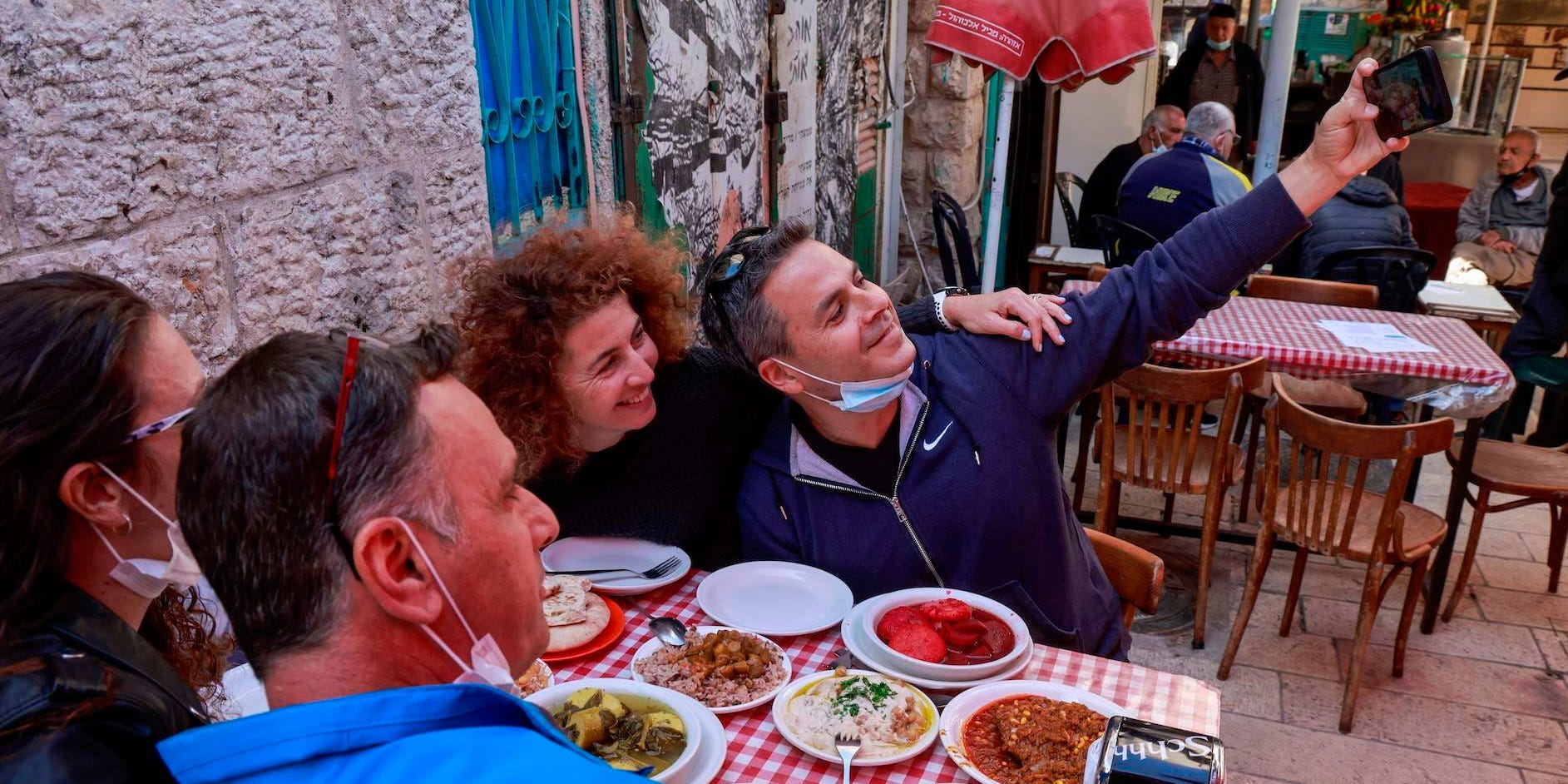 People sitting around a table in a restaurant requiring Israel's green pass huddle to take a group selfie.