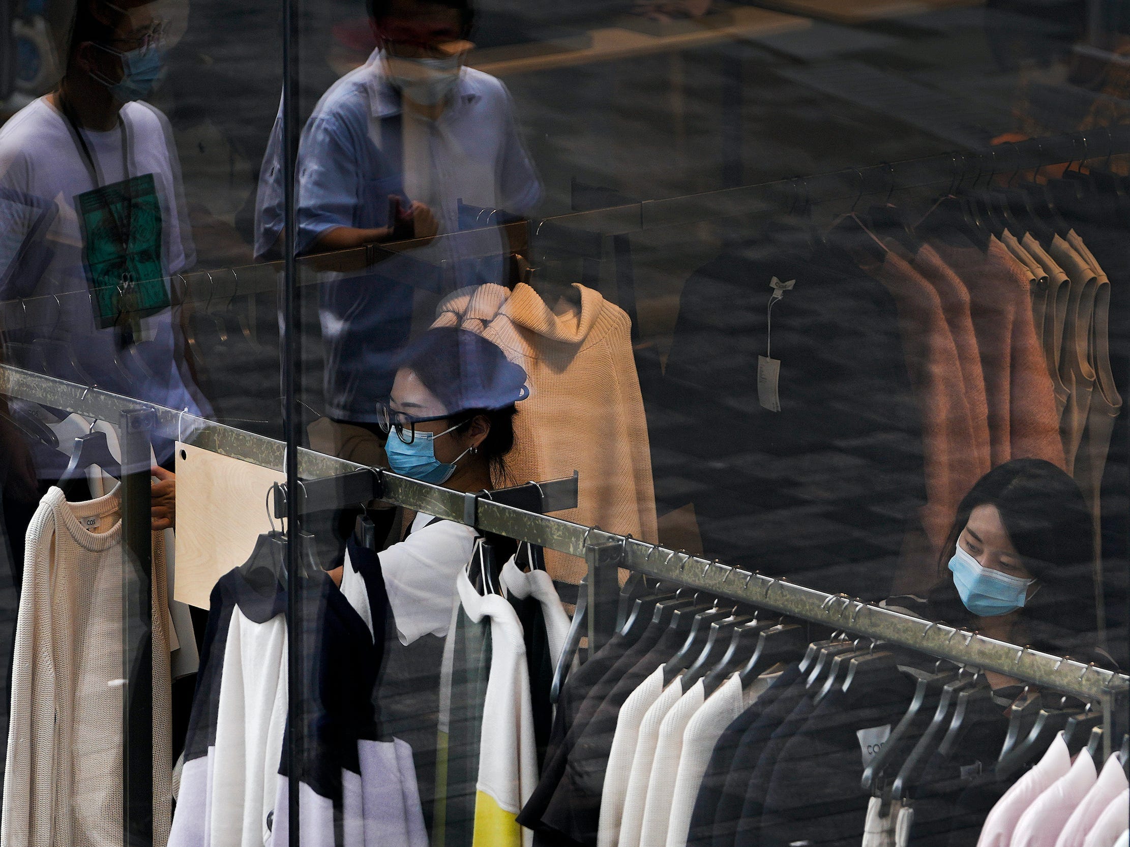 Two women wearing face masks shop for clothes