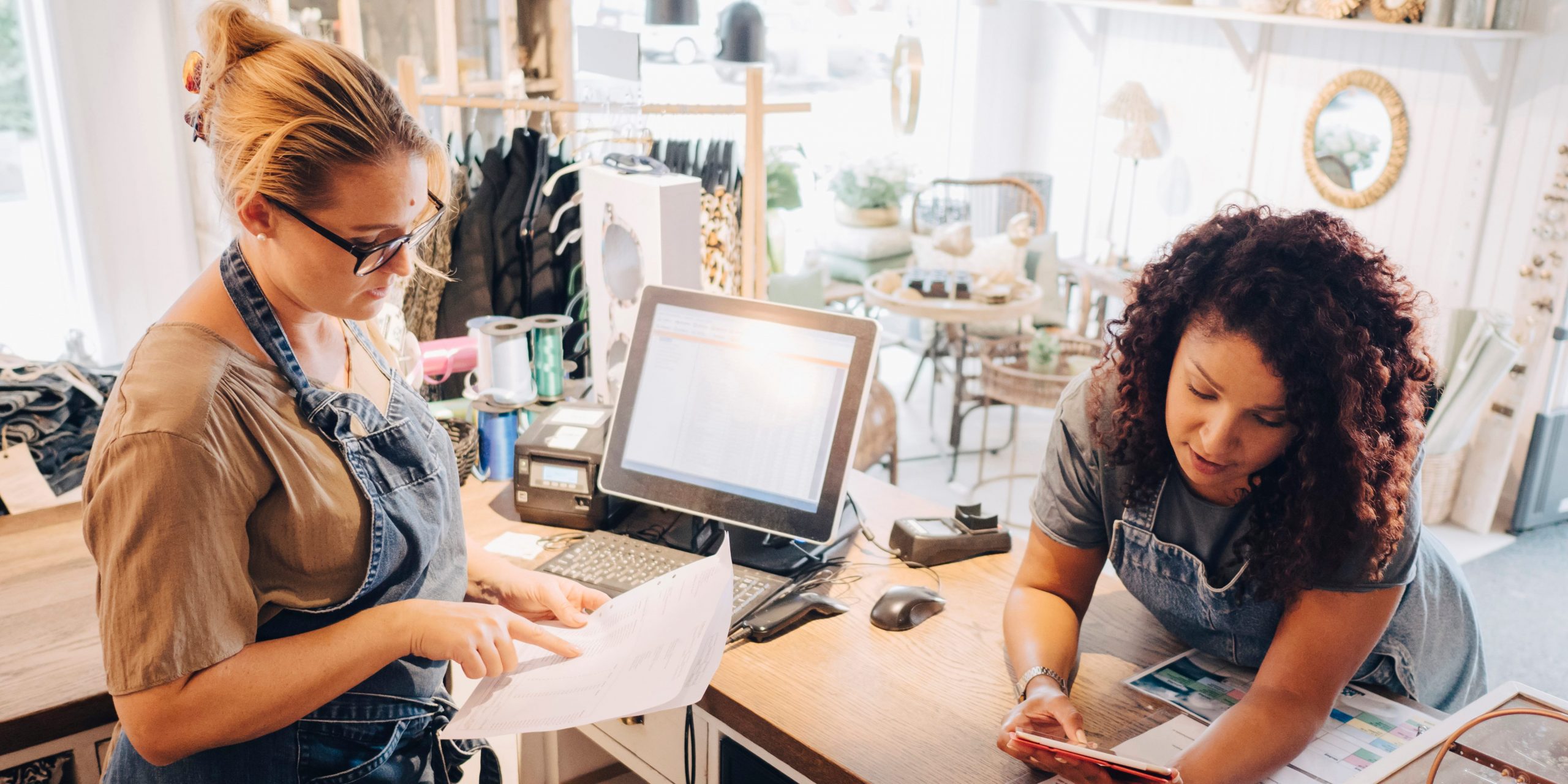 Colleagues discussing over financial receipt with digital tablet at checkout counter in store.