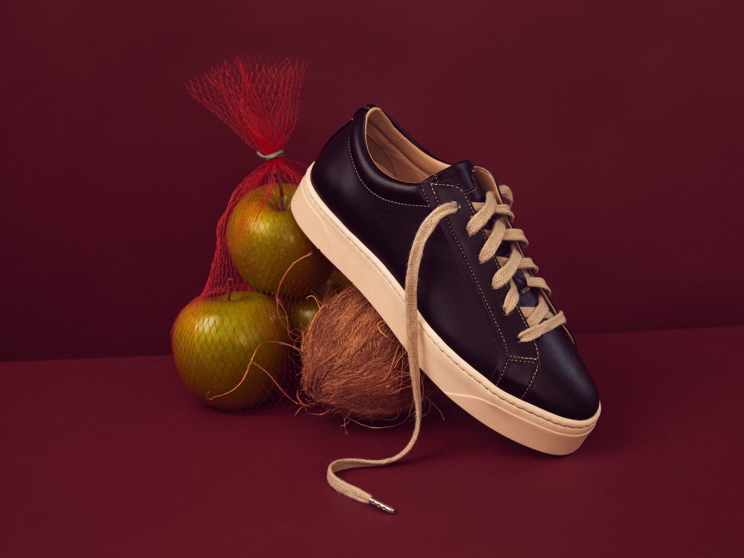 a black shoe propped up by apples on a red table