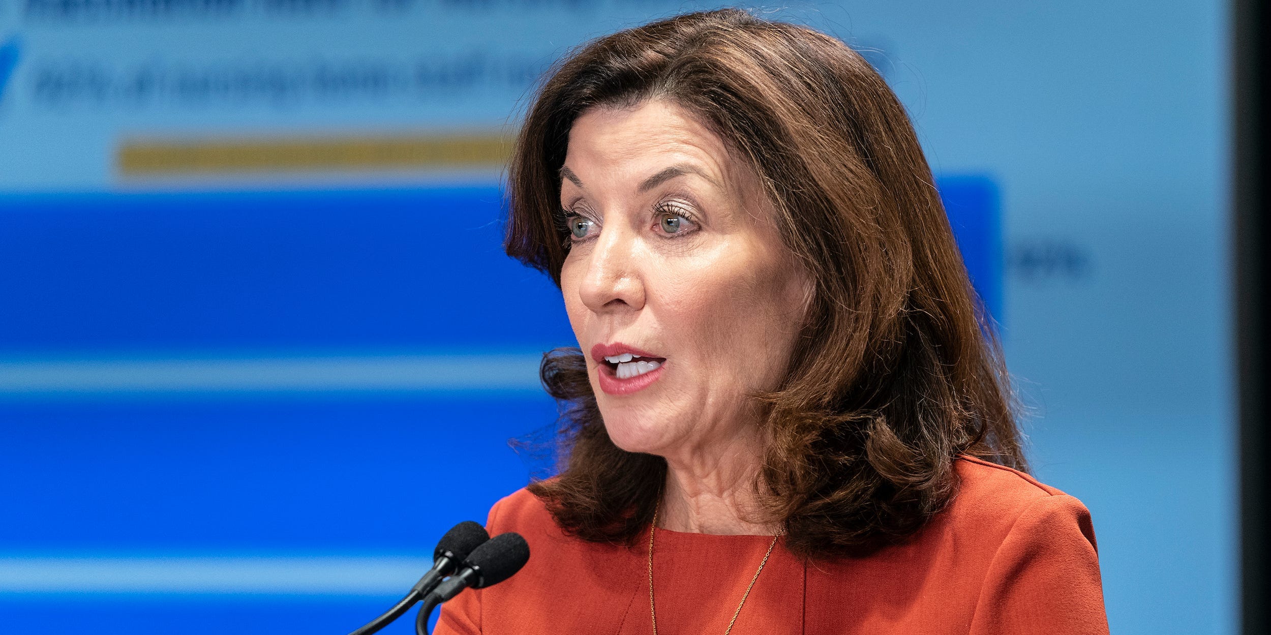 New York Governor Kathy Hochul speaks in front of a powerpoint presentation at a briefing.