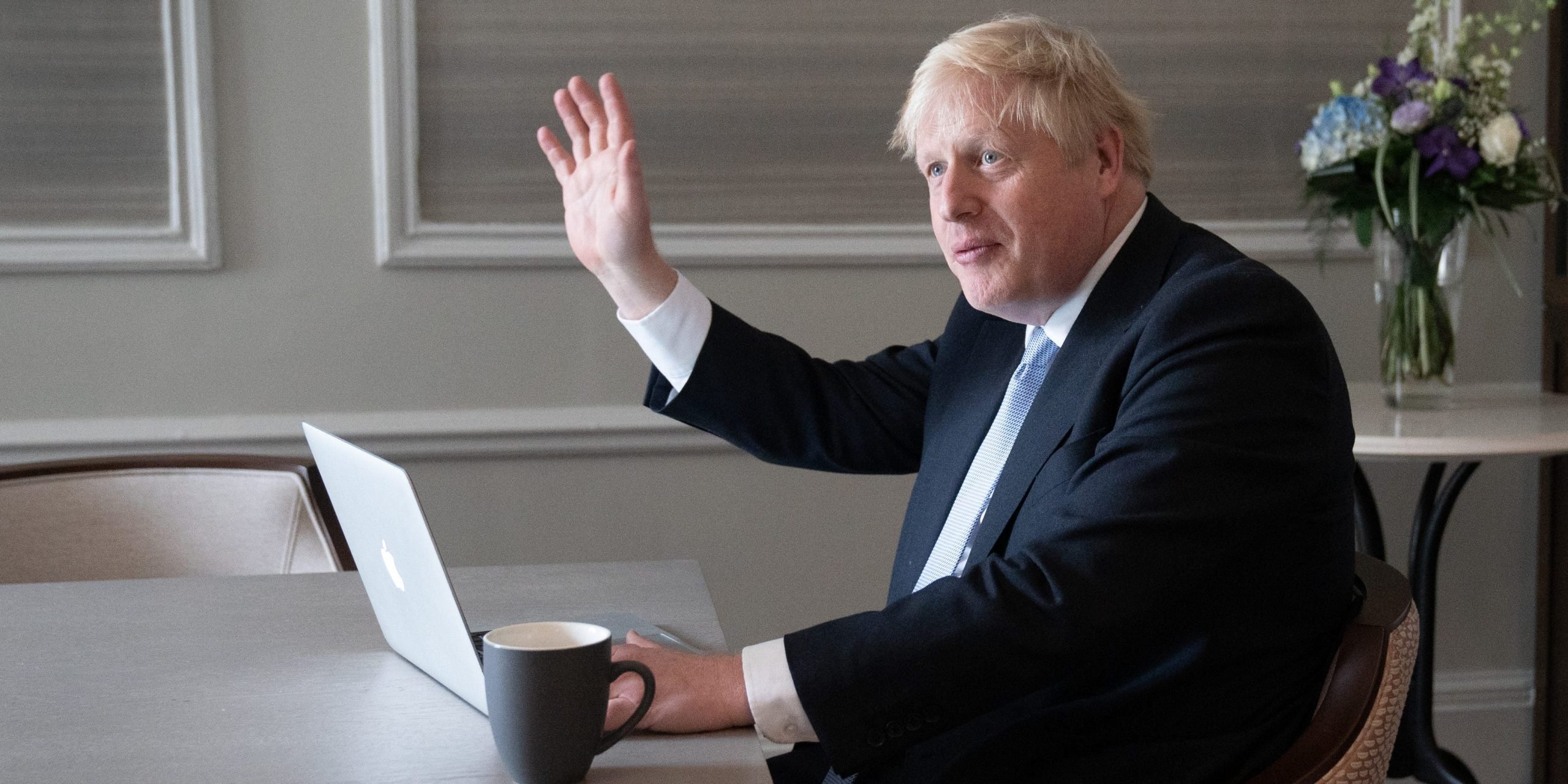 Boris Johnson waving, sat at a desk with a laptop