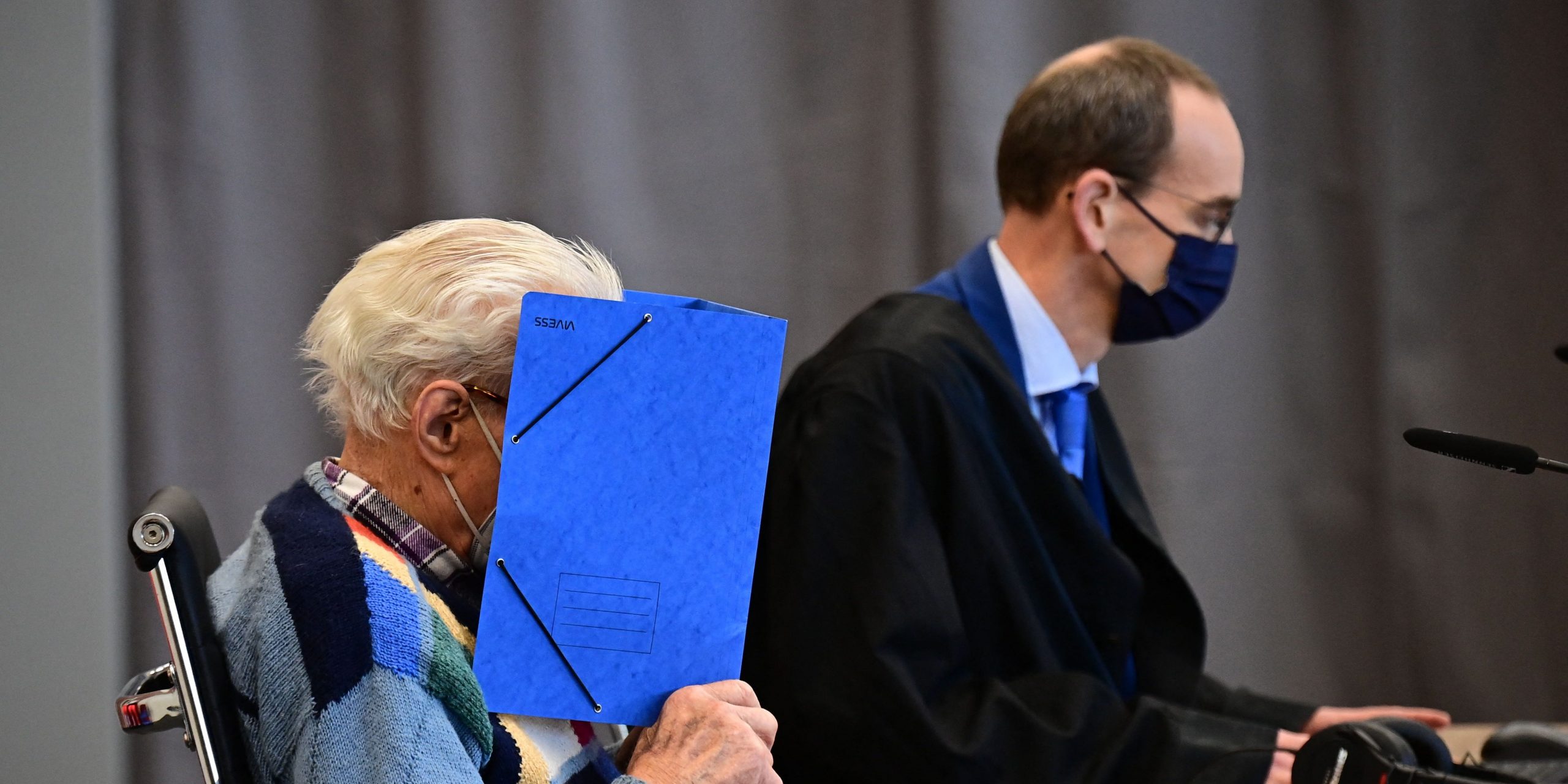 Defendant Josef S. sits while holding a blue folder in front of his face.
