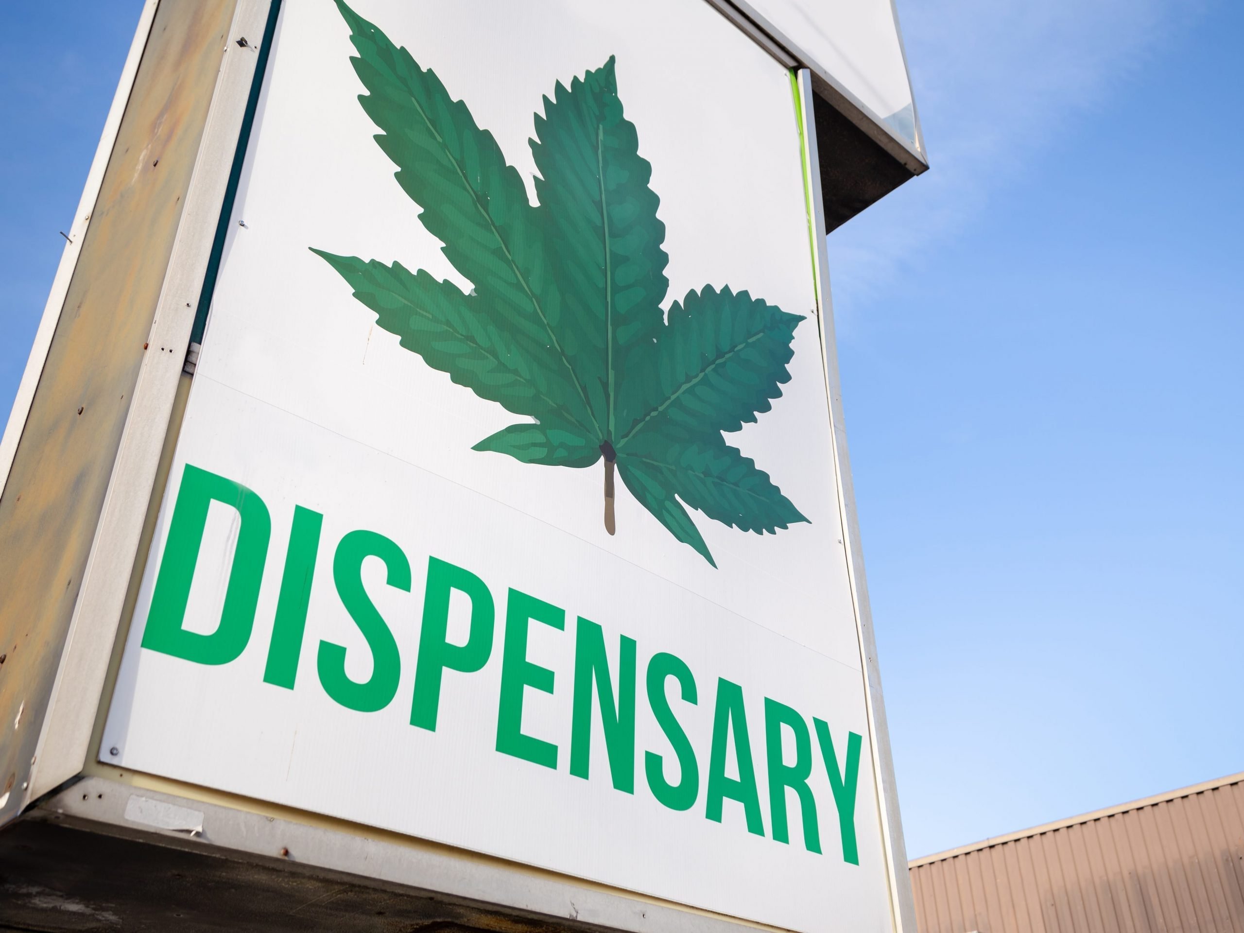 A white sign with green letter and a marijuana leaf that reads "dispensary"