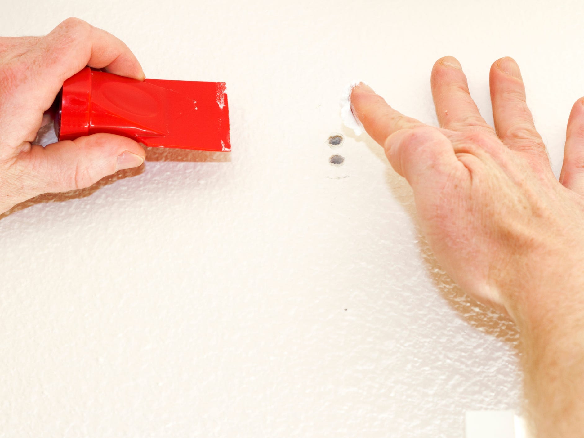 A pair of hands filling in screw holes with drywall compound