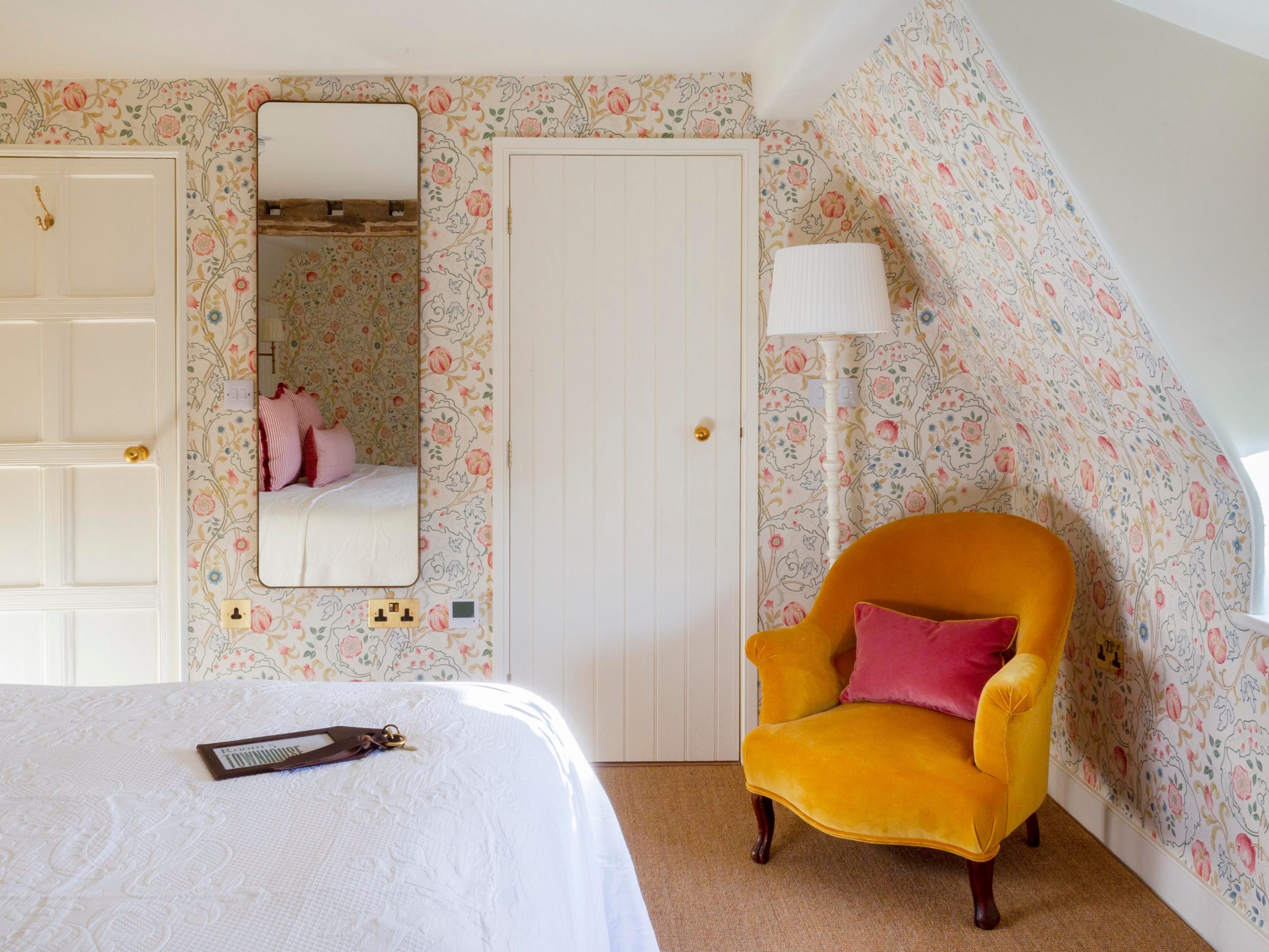 A yellow armchair in the corner of a room with patterned wallpaper.