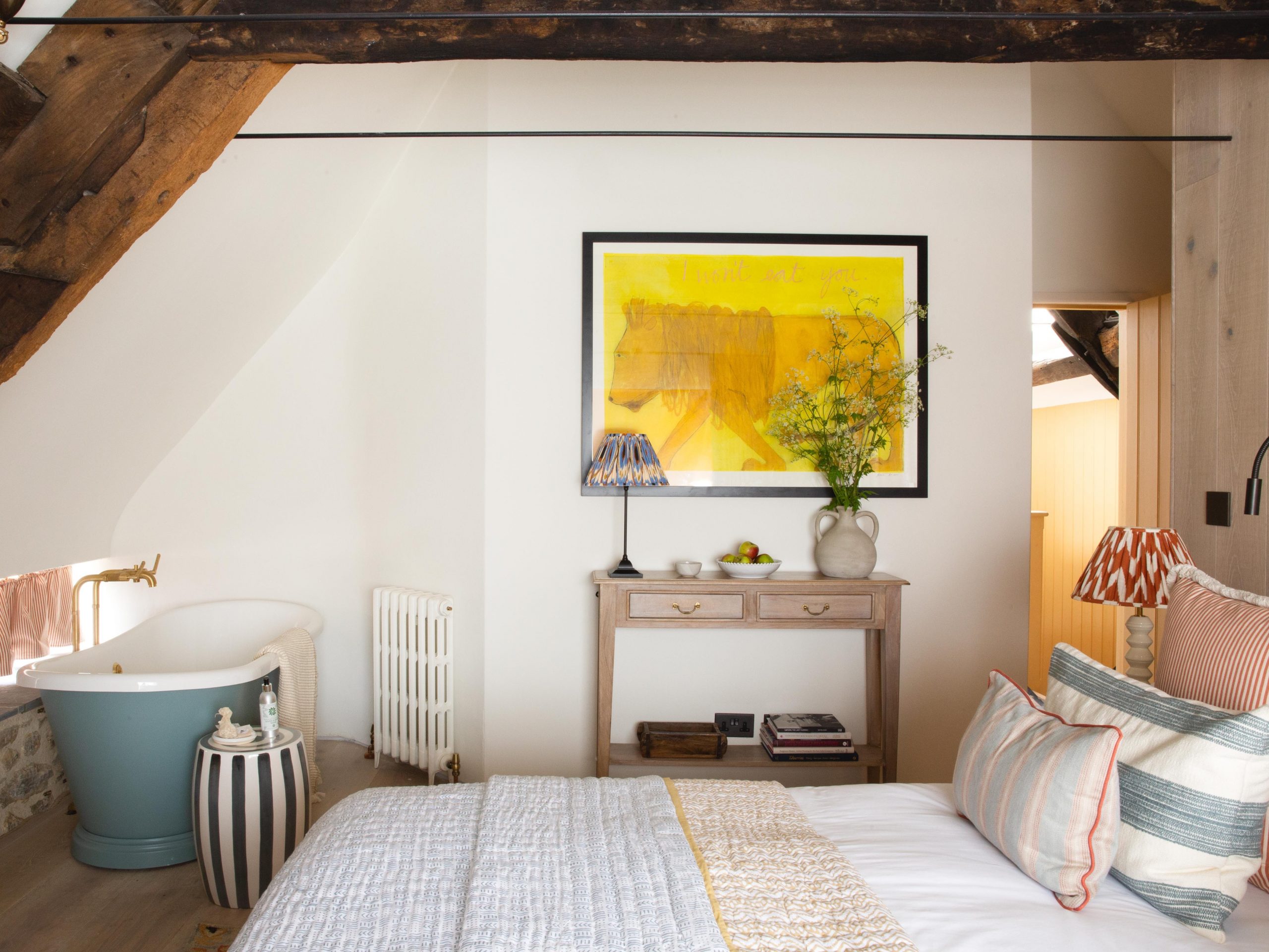 A bed in a white room with exposed wood beams.