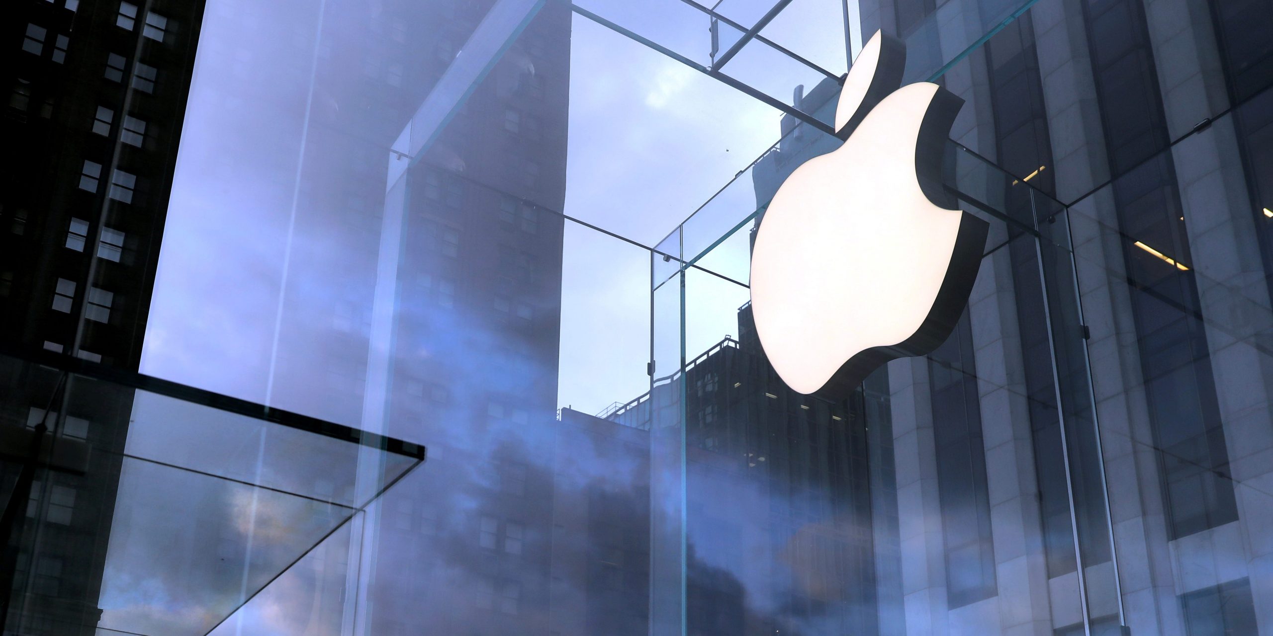 A cloudy sky behind a brightly lit Apple logo in a Manhattan store