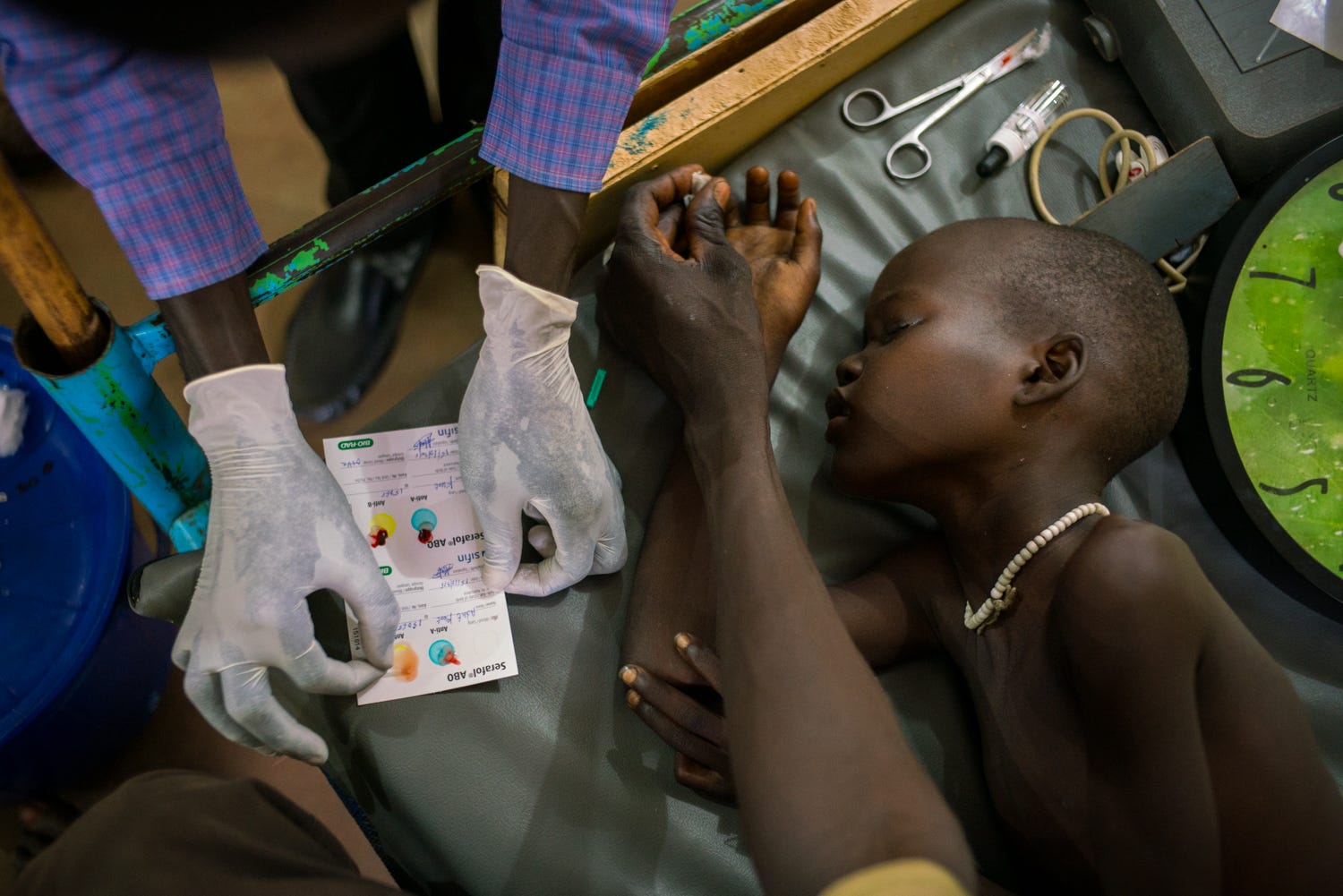 An 8-year-old boy receives treatment for cerebral malaria by nurses, whose hands are visible around his body.