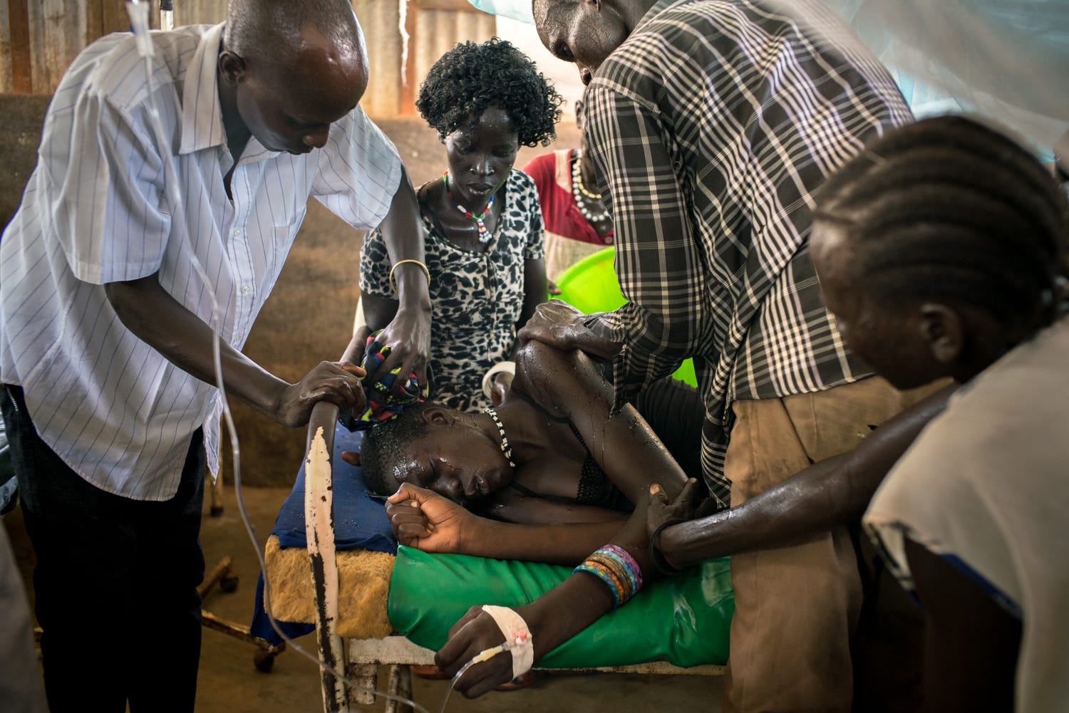 A nurse uses a wet compress to a patient as others hover over him to offer comfort.