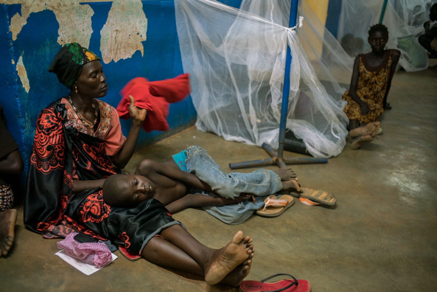A mother sits on the ground as she fans her feverish child.
