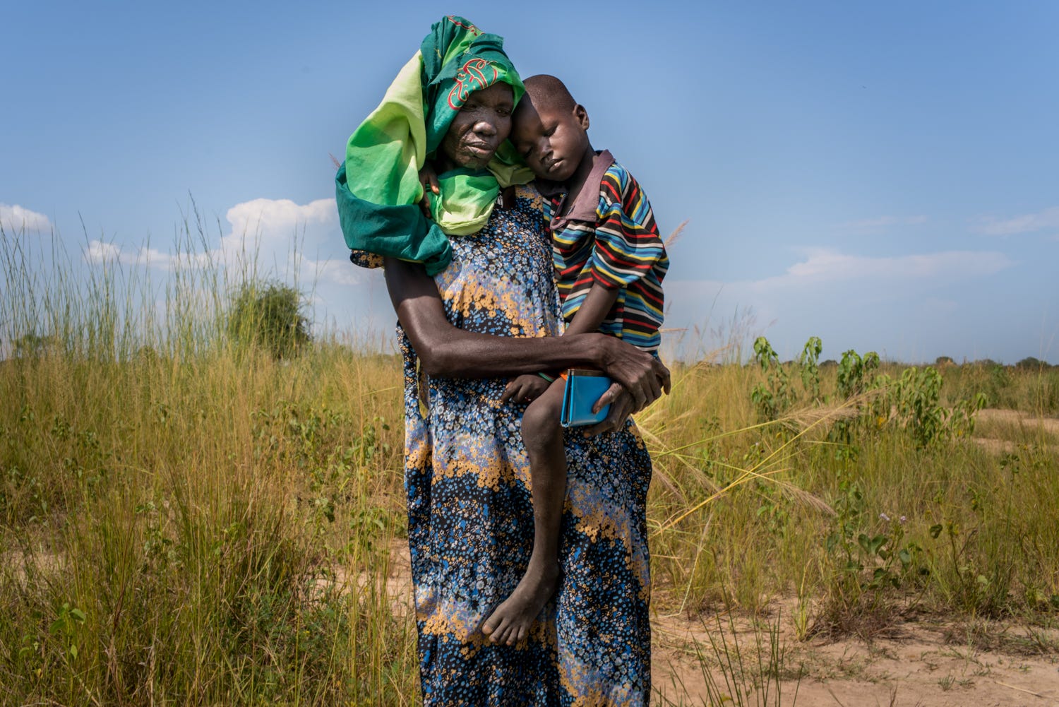 A woman is seen walking as she carries her sick child.