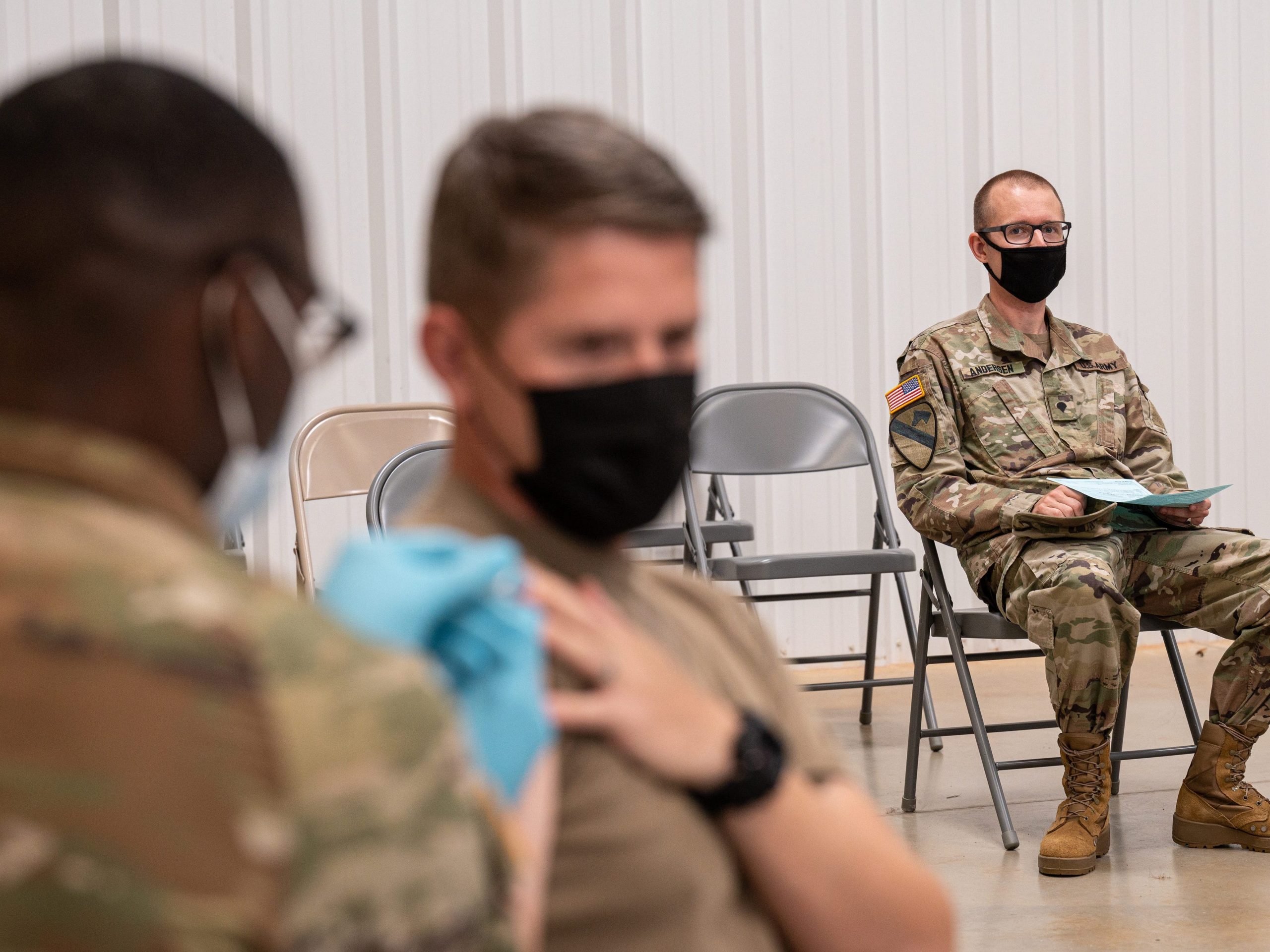 A soldier watches another soldier receive his COVID-19 vaccination.