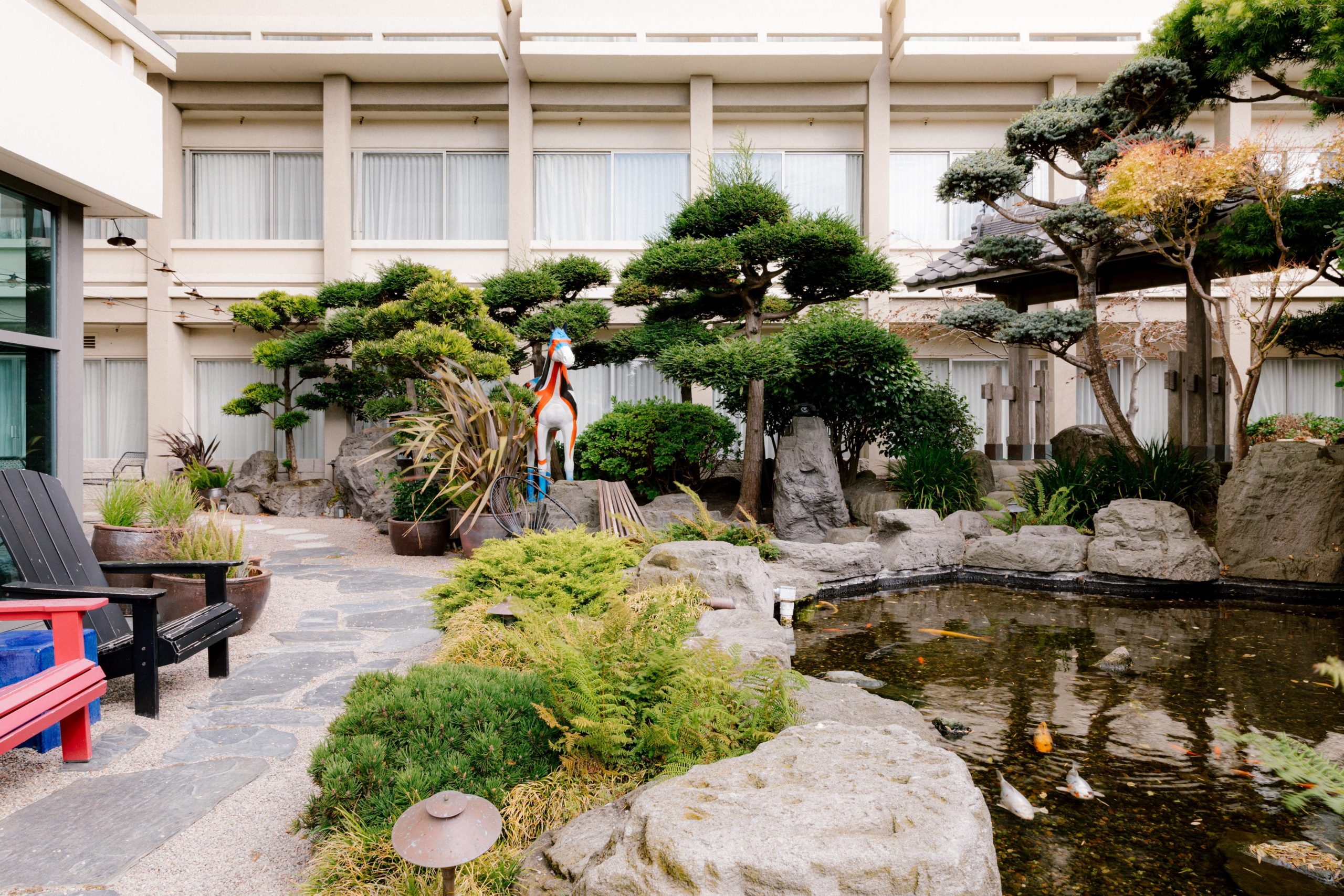 An outdoor area at Hotel Kabuki with lounge chairs, trees, and a pond with fish.