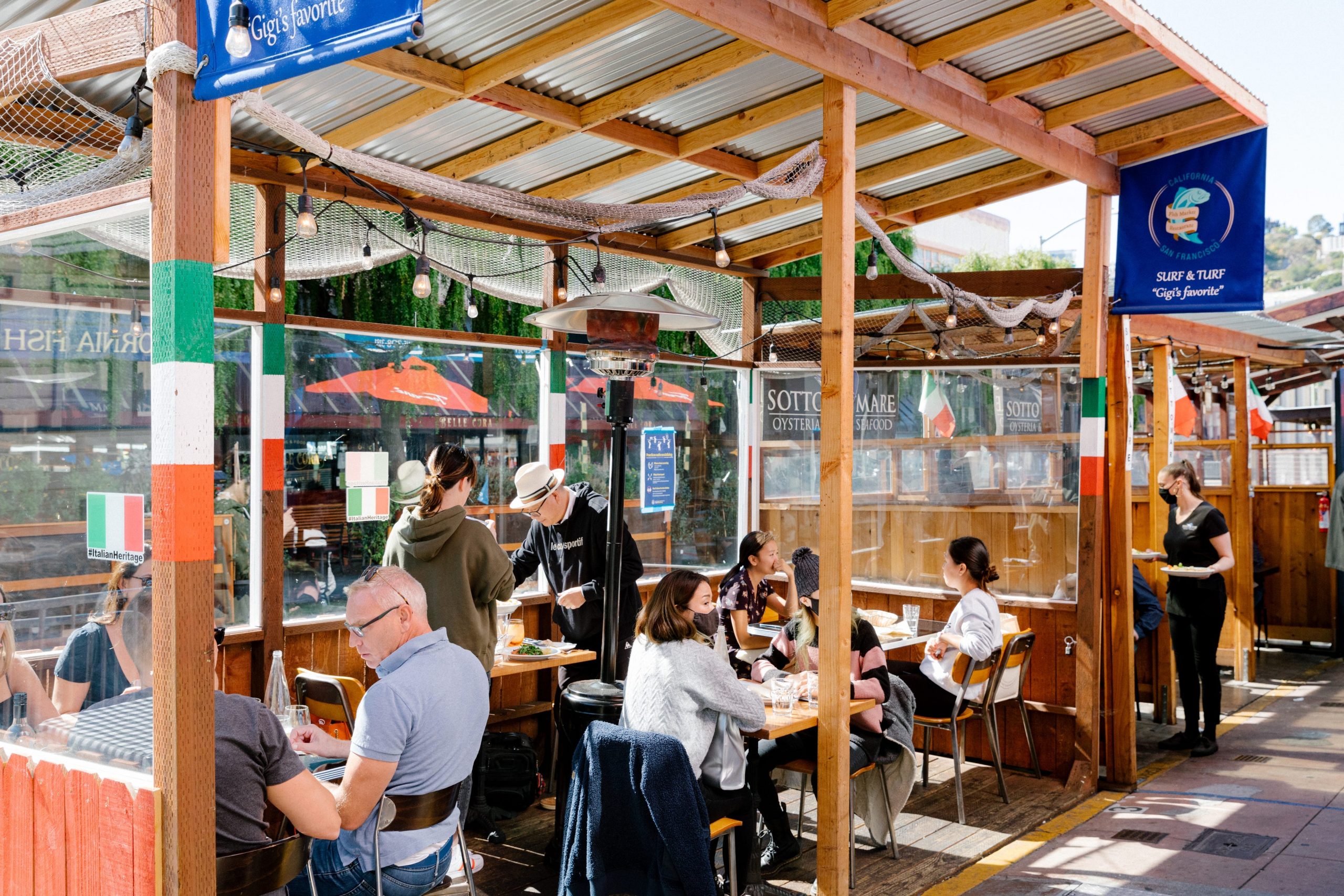 Patrons at San Francisco's California Fish Market sit in an outside patio area adorned in Italian flags while waiters serve them food.