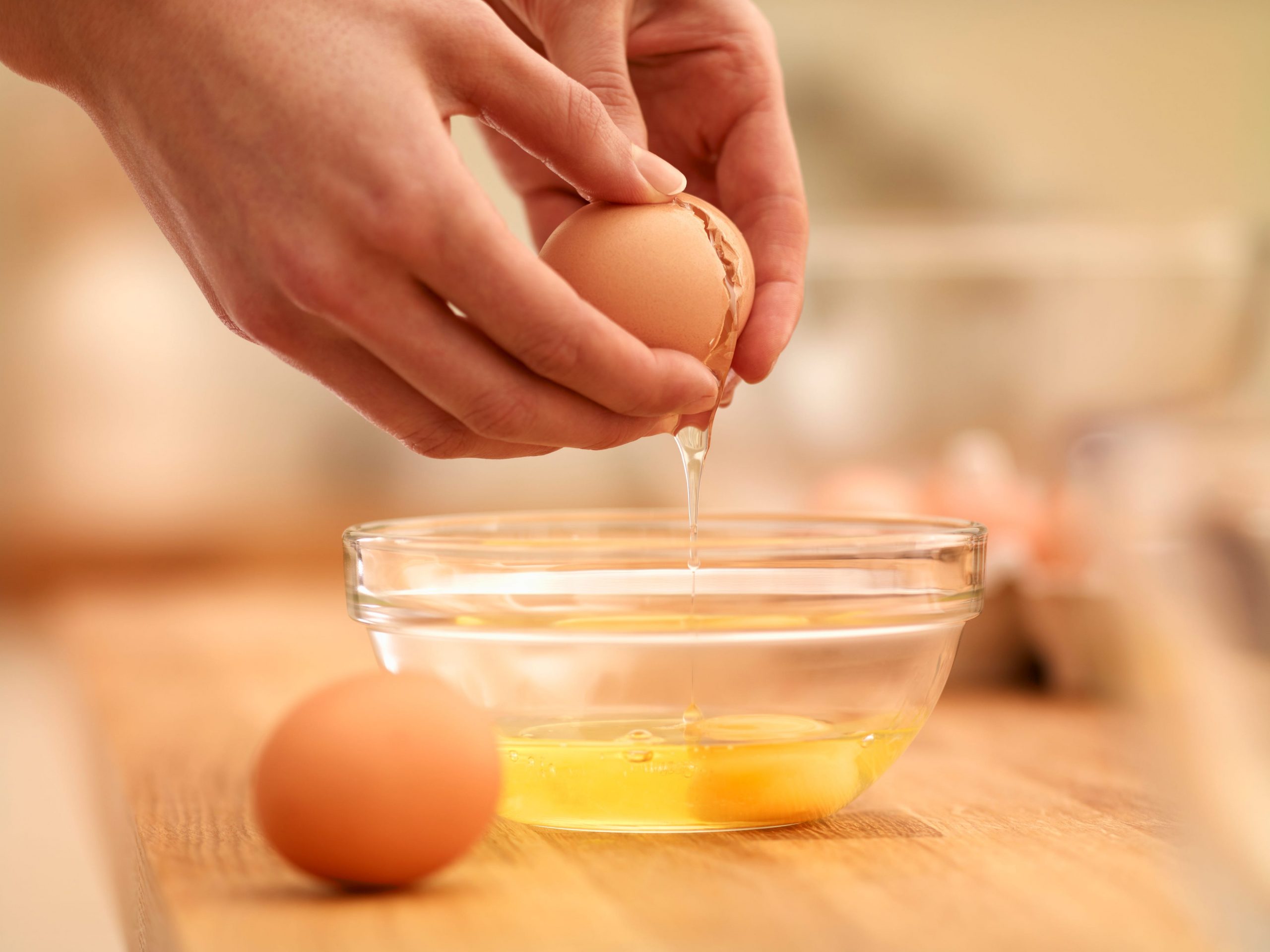 A person cracks a raw egg into a glass bowl.