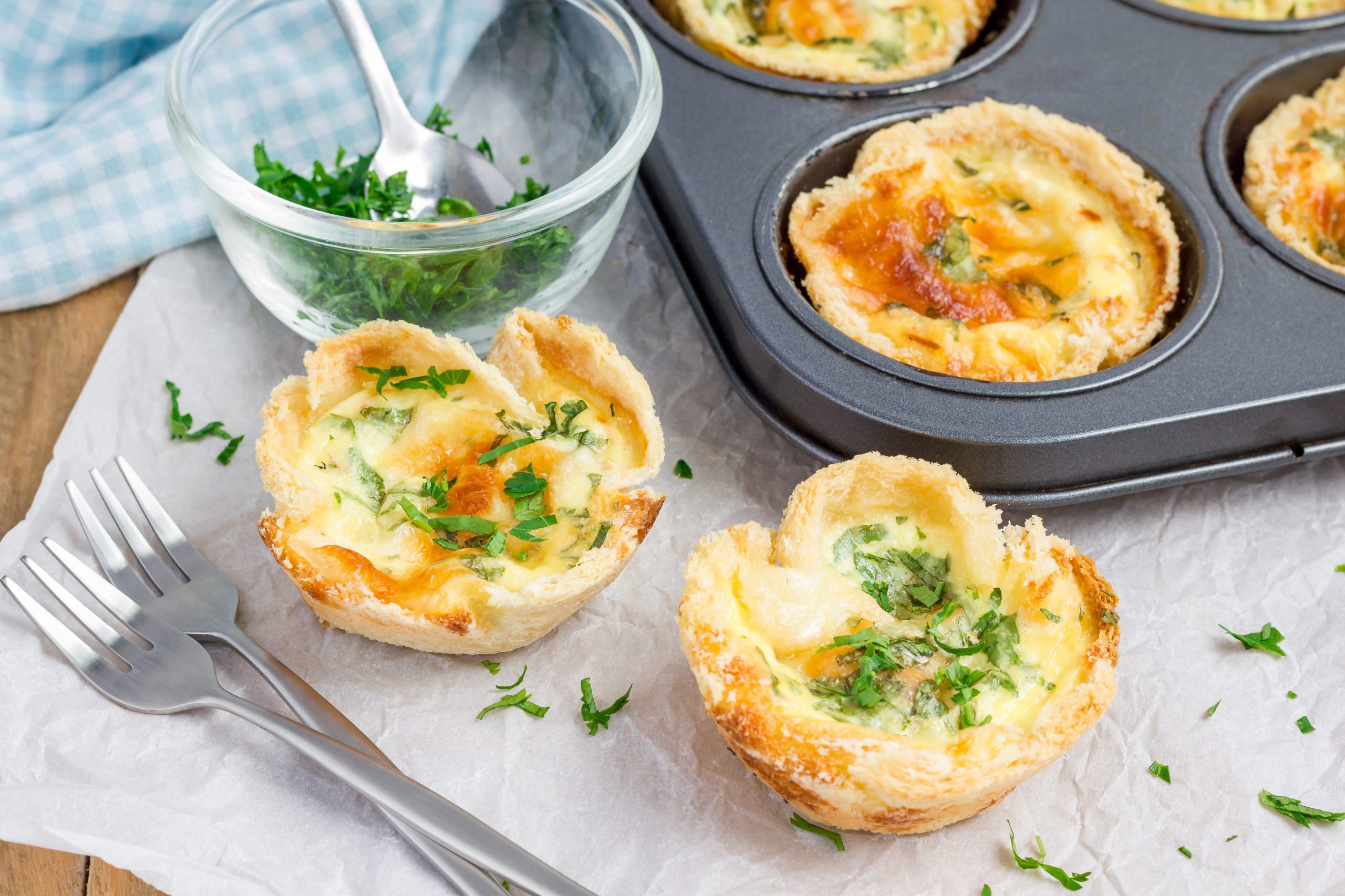 A photo of two egg muffins sitting on a counter next to a muffin tin holding more egg muffins.